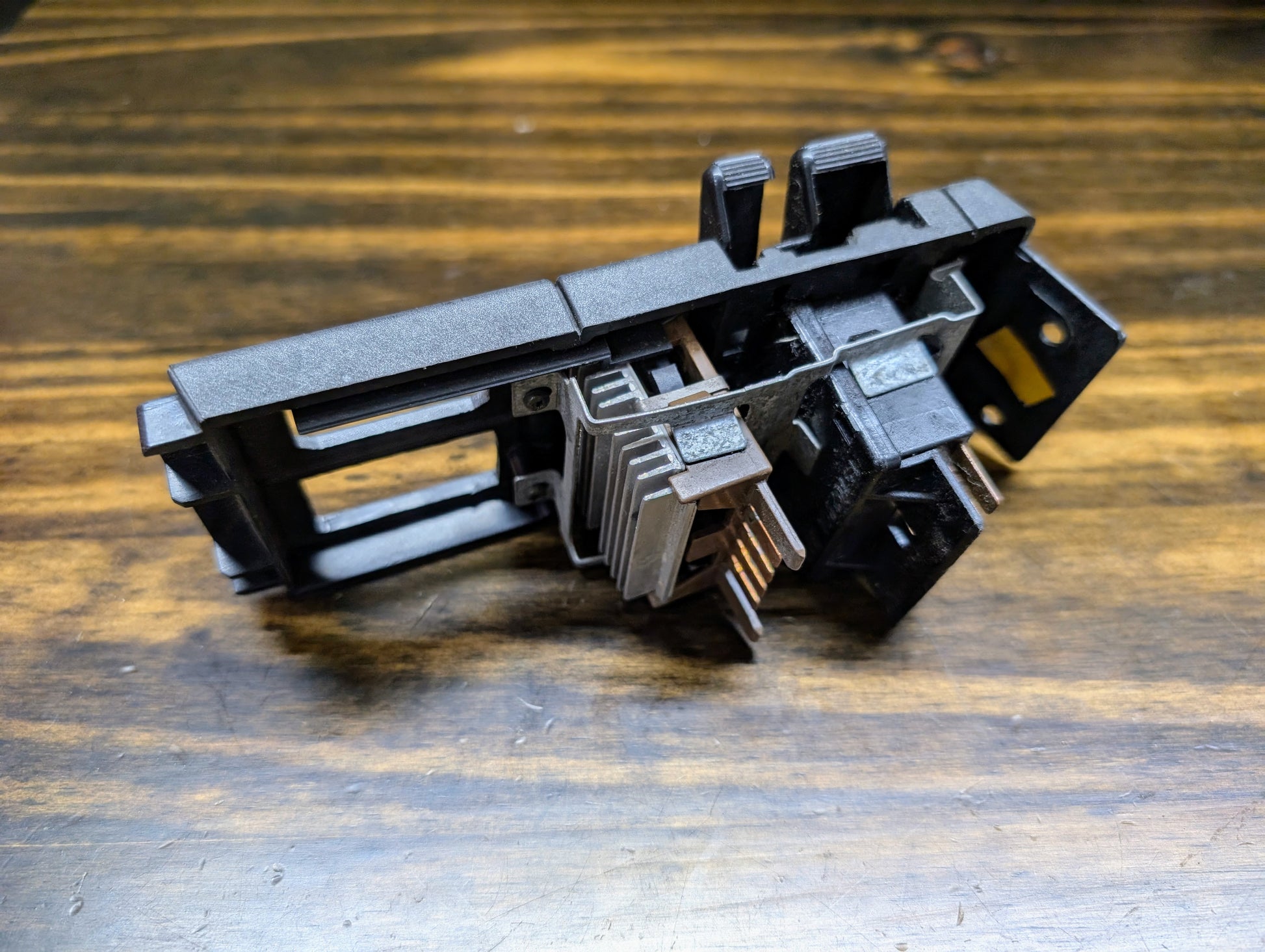 A close-up of a General Motors OEM Headlight Headlamp Switch for 1986-1994 Chevy S10, Blazer, GMC S15, and Jimmy, featuring multiple prongs and black plastic metal construction, shown on a wooden surface.