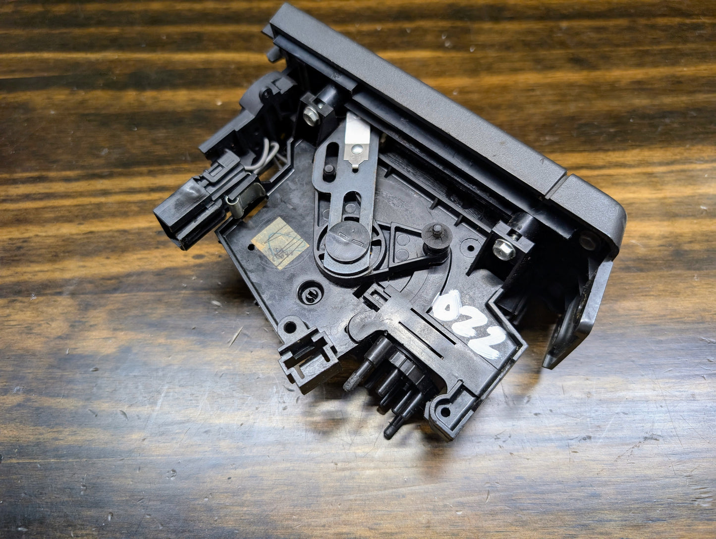 A close-up of a General Motors HVAC Heater Control Panel with A/C for 1986-1994 Chevrolet S10, Blazer, and more rests on a wooden surface. The black plastic part labeled 022 features visible gears and levers.