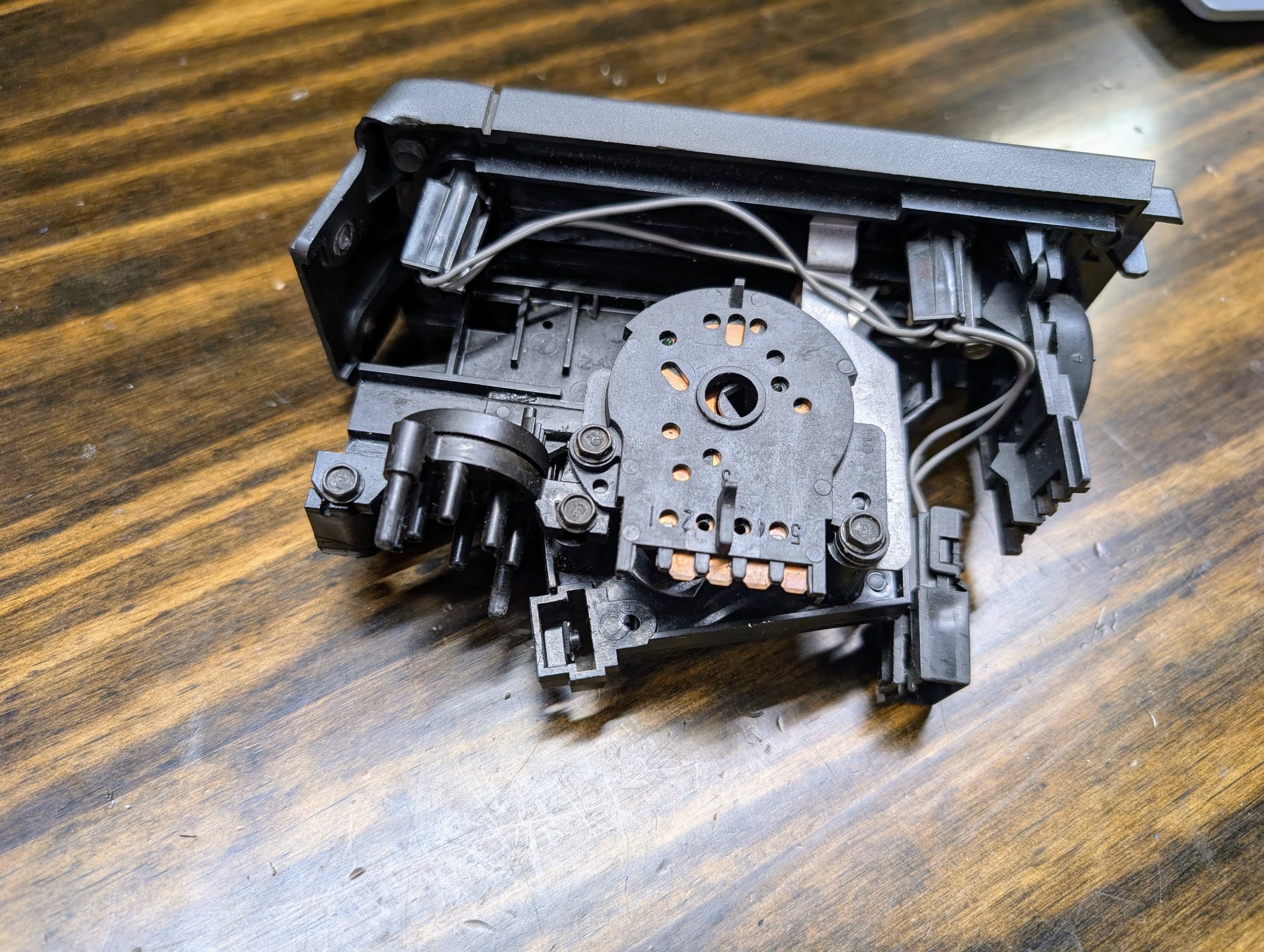 A close-up of a disassembled General Motors HVAC Heater Control Panel with A/C for 1986-1994 Chevrolet S10, Blazer, and more, showing wires and connectors on a wooden surface with visible grain.