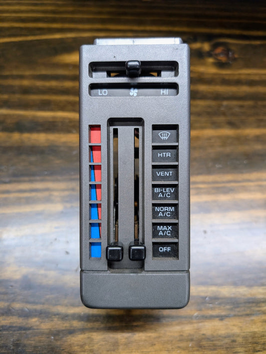 A General Motors HVAC Heater Control Panel with A/C for 1986-1994 Chevrolet S10, Blazer and more, features temp/fan sliders (blue to red) and buttons: HTR, VENT, BI-LEV A/C, NORM A/C, MAX A/C, OFF; shown on a wooden surface.