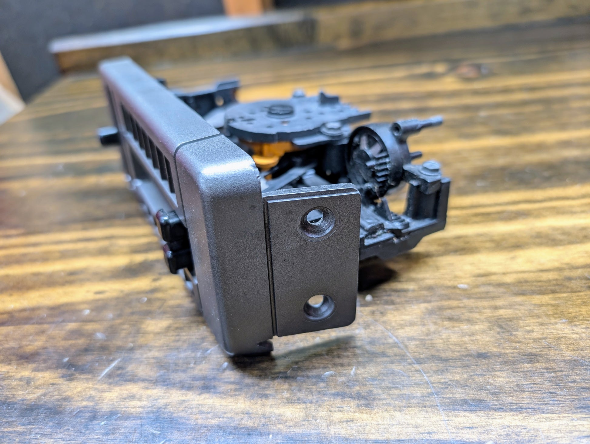 A close-up of a General Motors HVAC Heater Control Panel with A/C for 1986–1994 Chevrolet S10 and Blazer, showing gears and holes, is placed on a wooden surface. This component is part of the vehicles climate control system.