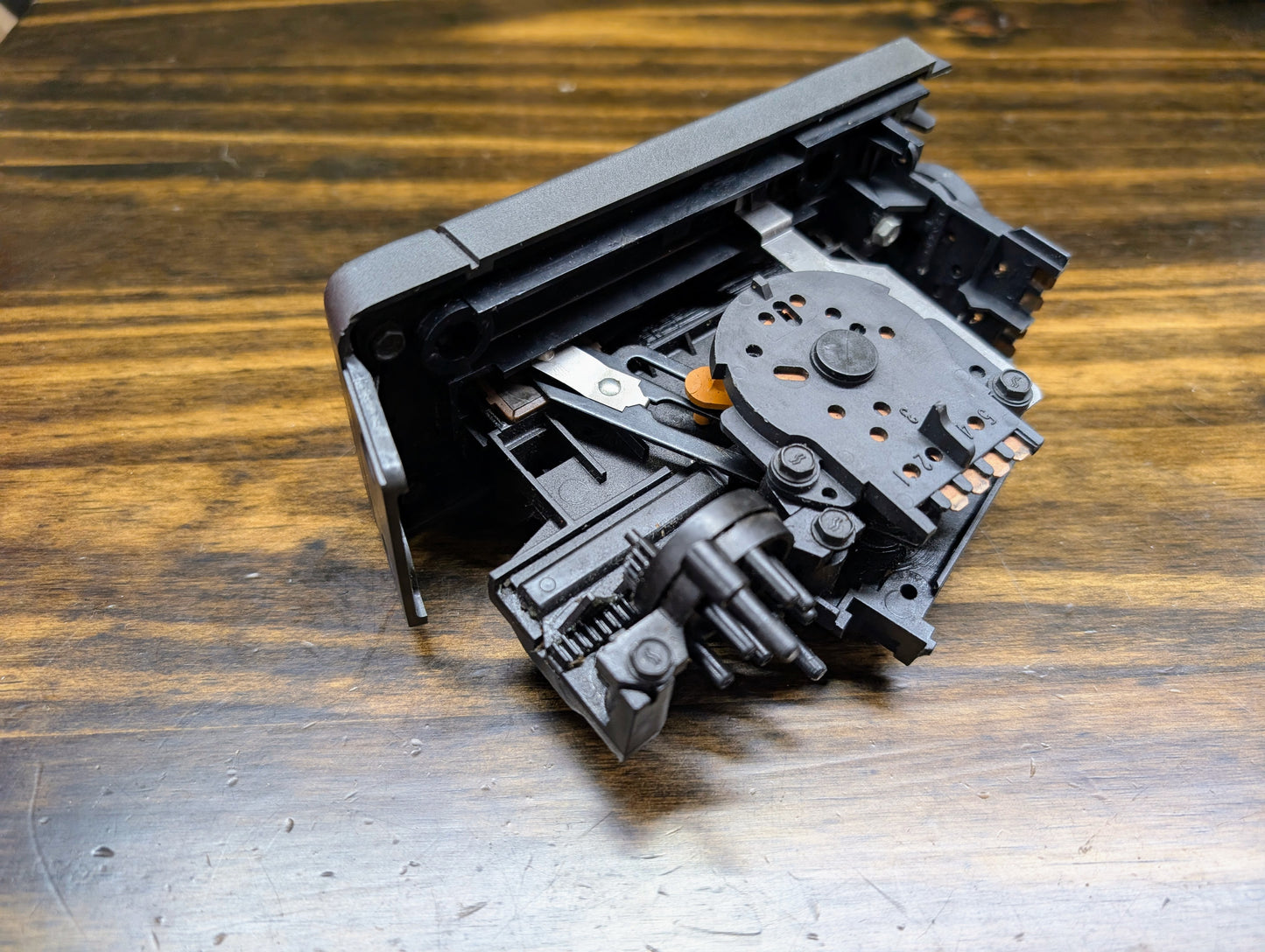 A close-up of a black General Motors HVAC Heater Control Panel with A/C for 1986–1994 Chevrolet S10 and Blazer, featuring gears and levers, resting on a wooden surface.