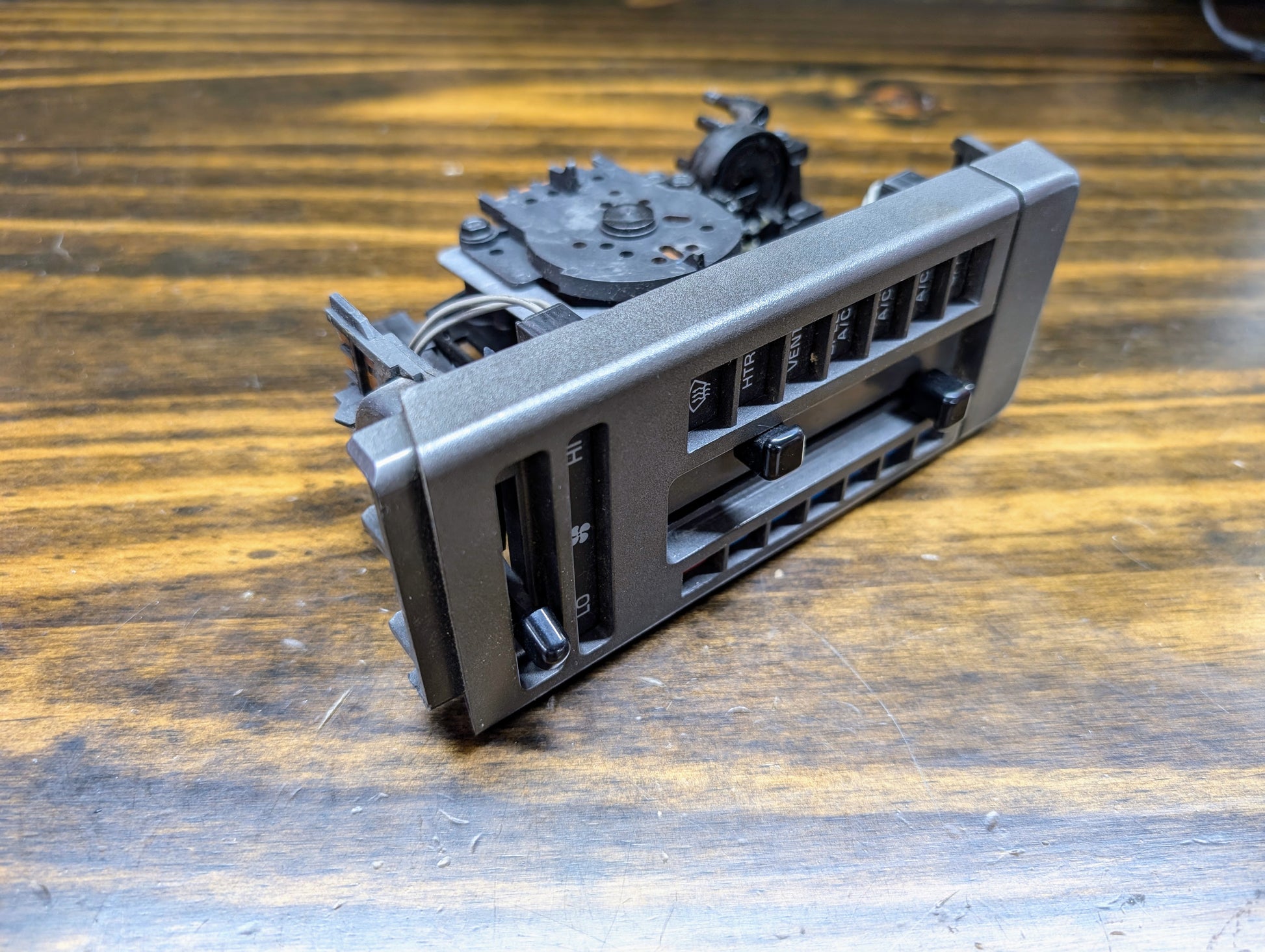 A General Motors HVAC Heater Control Panel with A/C for 1986-1994 Chevrolet S10 and Blazer is removed from its original position and placed on a wooden surface.