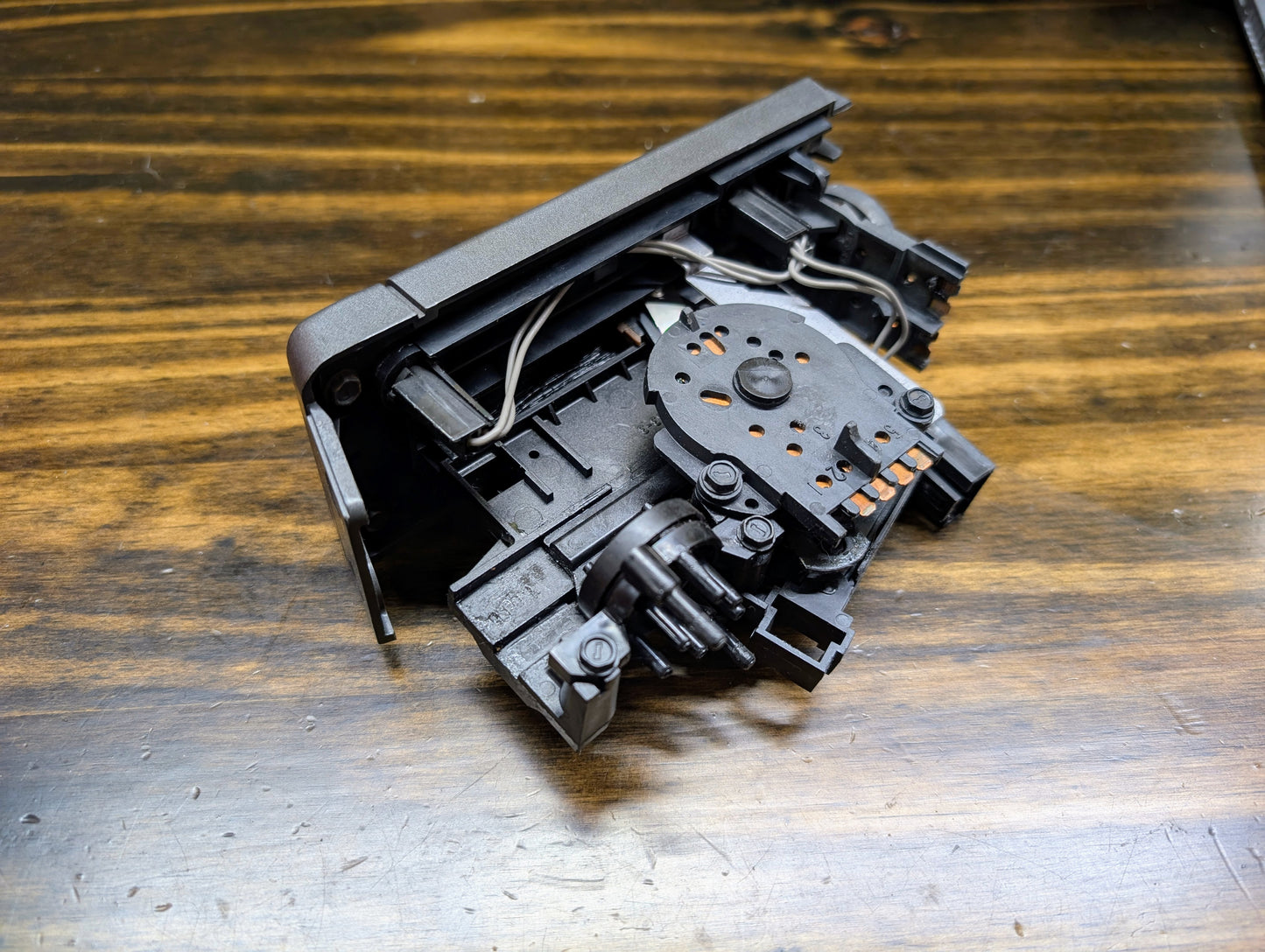 A close-up of a General Motors HVAC Heater Control Panel with A/C for 1986-1994 Chevrolet S10, Blazer, and more, showing black mechanical parts with visible gears and wires on a wooden surface.