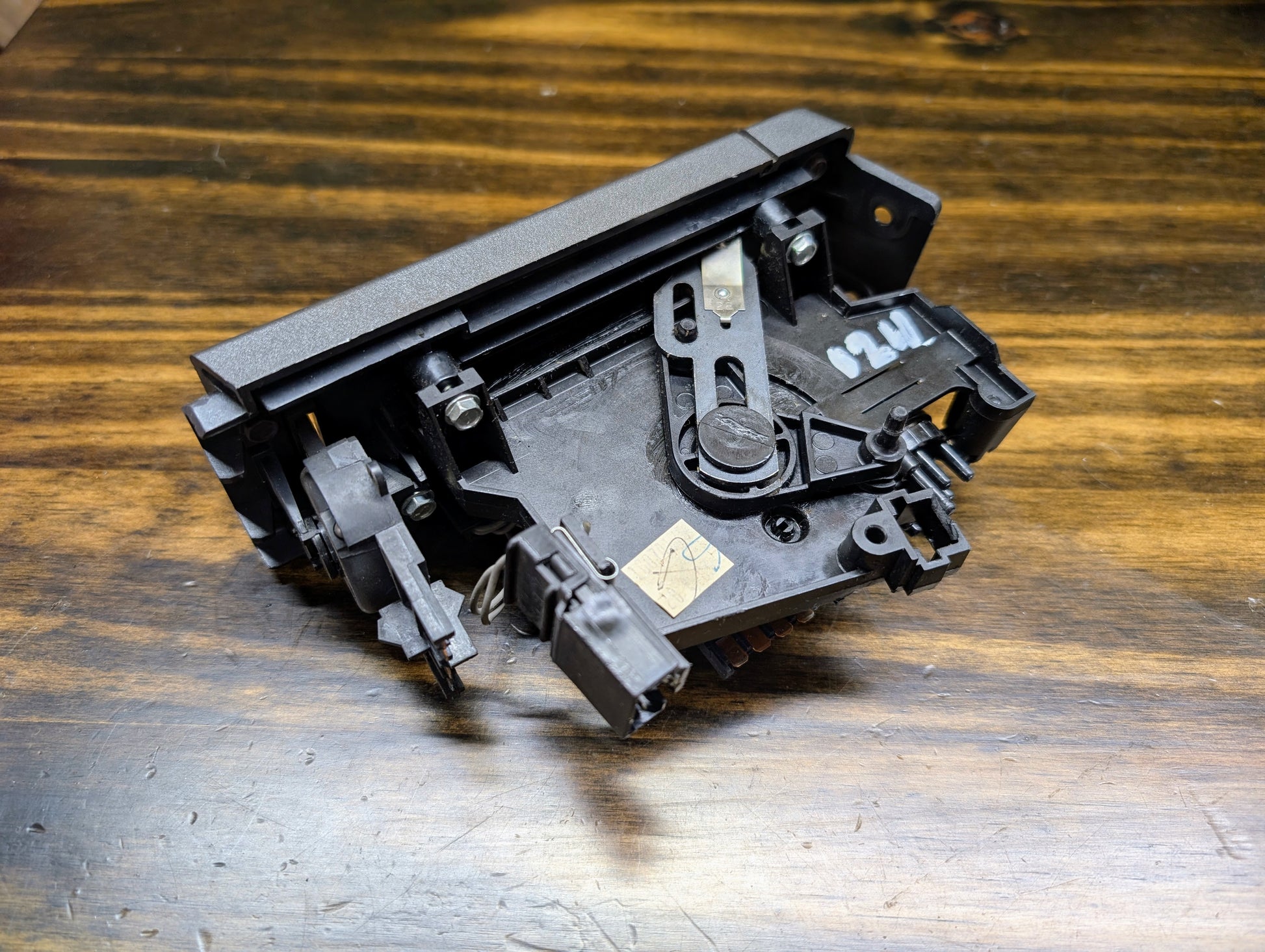 A close-up of a General Motors HVAC Heater Control Panel with A/C for 1986-1994 Chevrolet S10, Blazer, and more shows black plastic gears and levers on wood. The unit has 2261 numbering and a yellow sticker marked with an X.