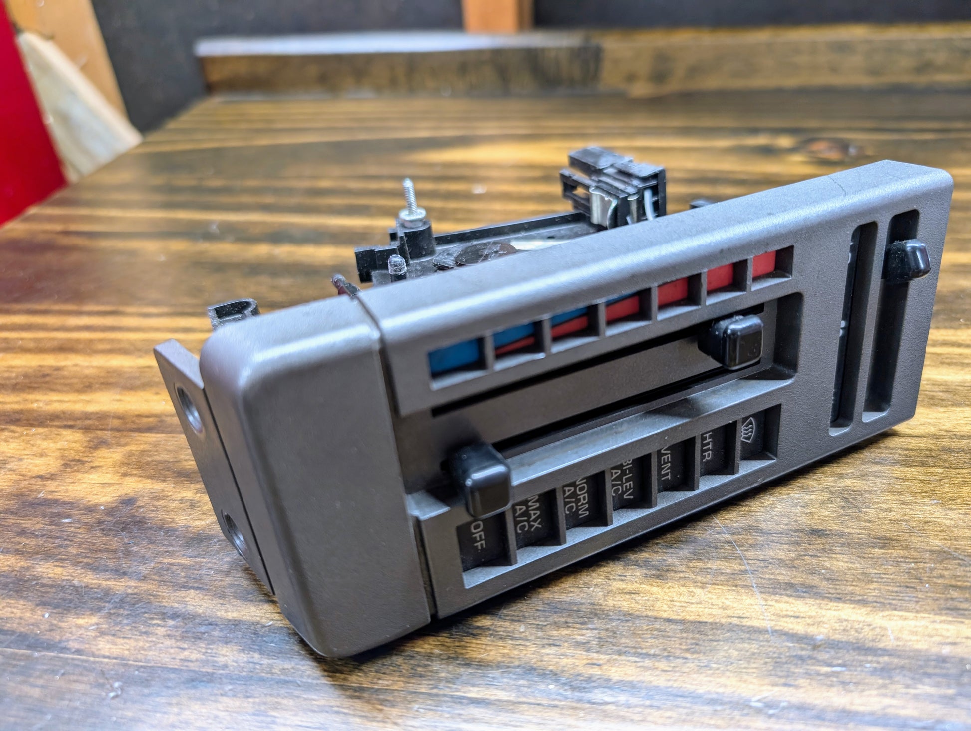 A close-up of a General Motors HVAC Heater Control Panel with A/C for 1986-1994 Chevrolet S10, Blazer, and more is shown on a wooden surface.