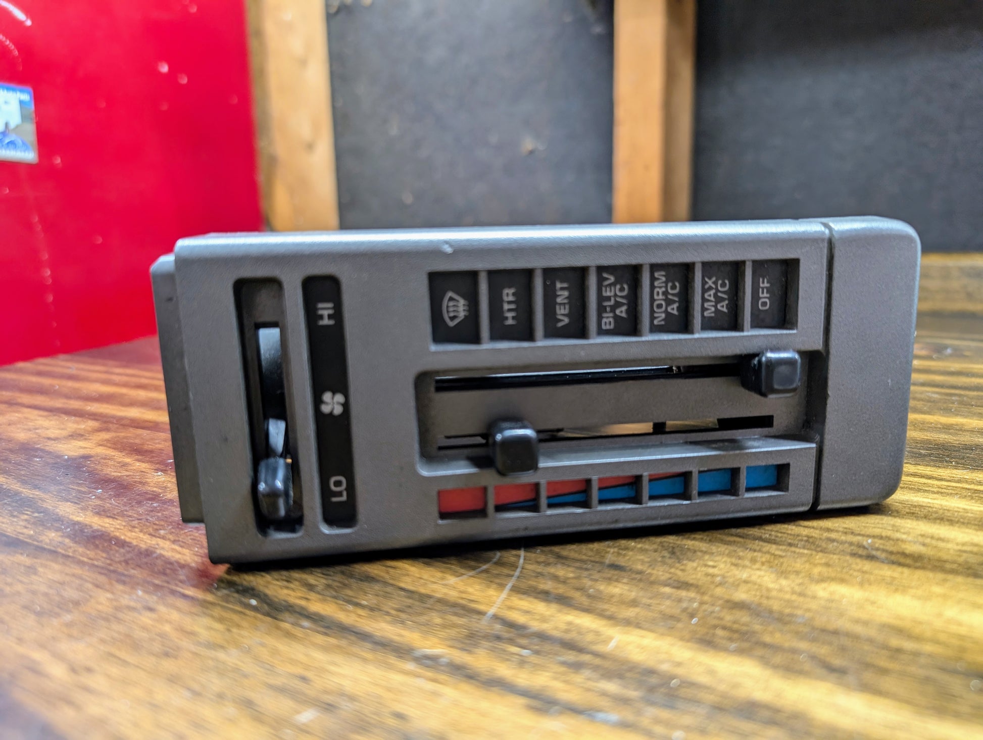 A General Motors HVAC Heater Control Panel with A/C, designed for 1986-1994 Chevrolet S10 and Blazer, is shown in close-up on a wooden surface, highlighting its sliders and buttons for fan speed, temperature, and air flow adjustment.