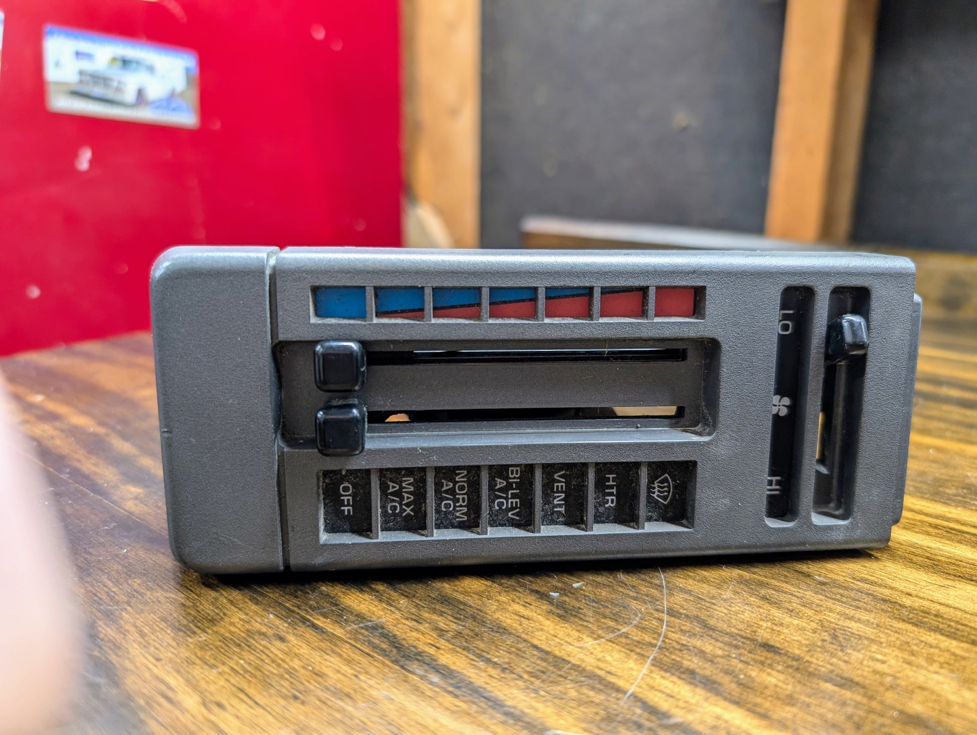 A General Motors HVAC Heater Control Panel with A/C for 1986-1994 Chevrolet S10, Blazer, and more, featuring black sliders/buttons and labeled fan, air direction, and AC settings, shown on a wooden surface.
