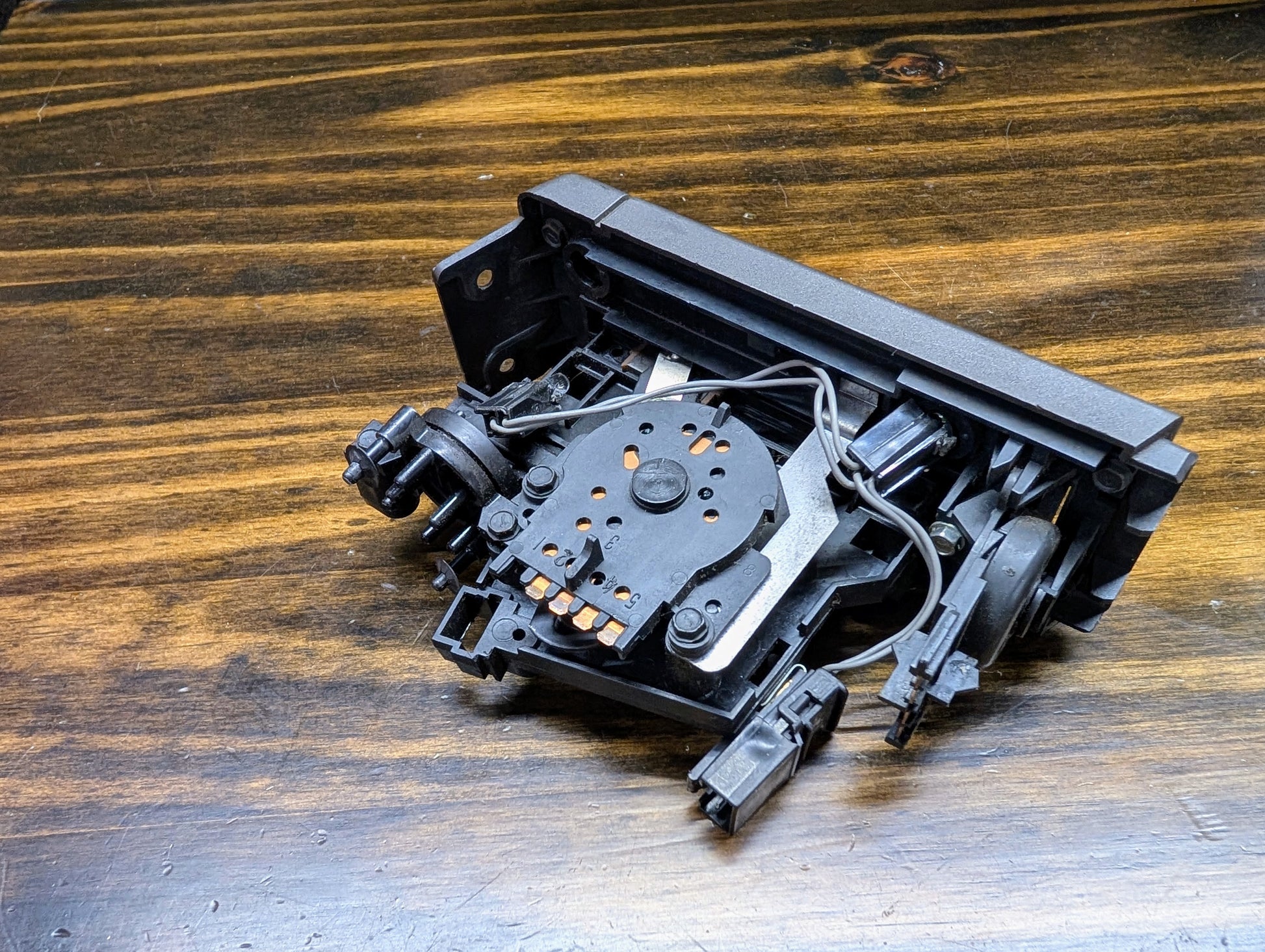 A disassembled CD/DVD drive rests on wood, revealing its laser and ribbon cables—much like examining a General Motors HVAC Heater Control Panel with A/C for 1986-1994 Chevrolet S10, Blazer, and more.