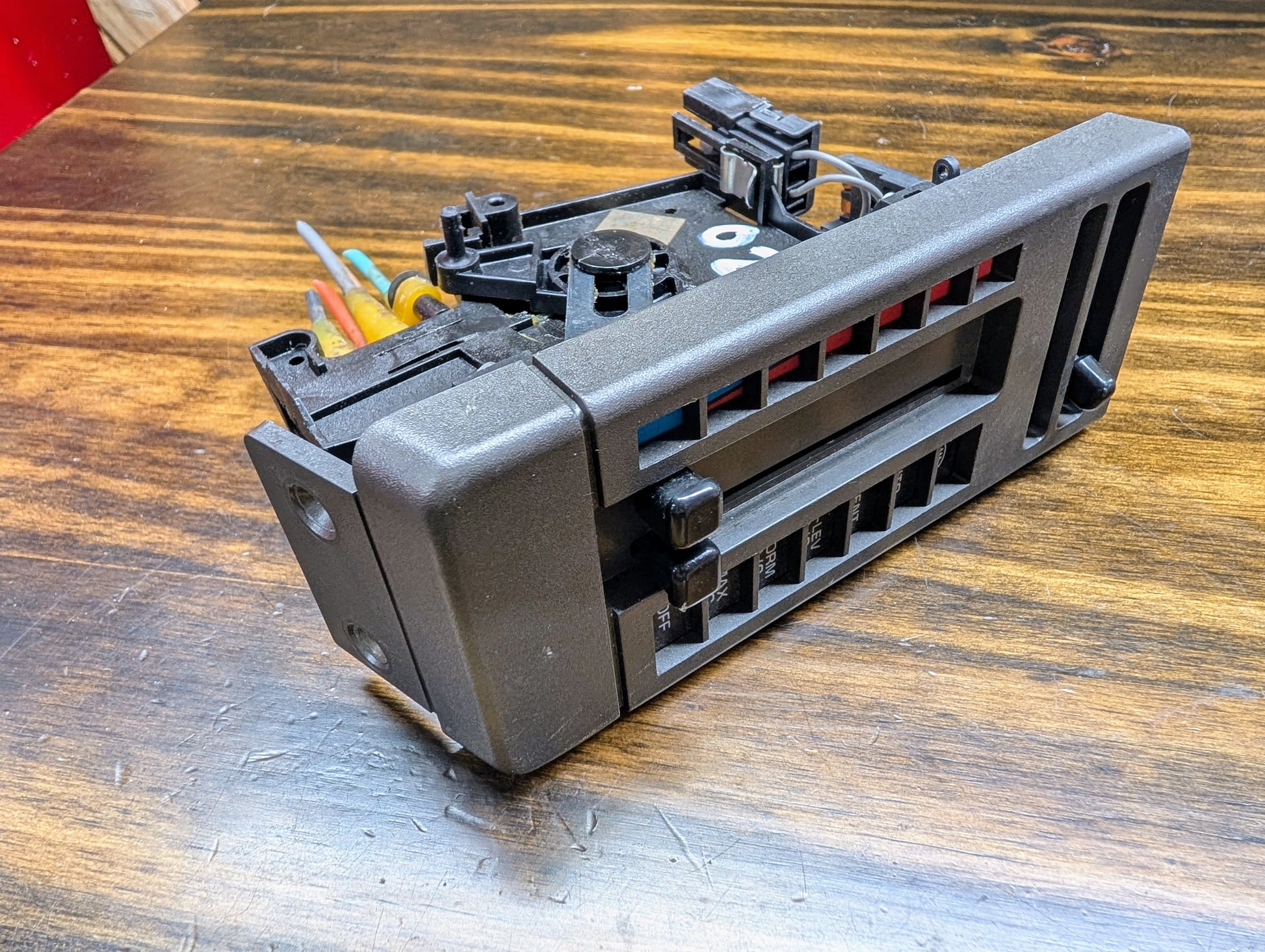 A General Motors HVAC Heater Control Panel with A/C for 1986-1994 Chevrolet S10 and Blazer rests on a wooden surface, with tools partially visible in the background.