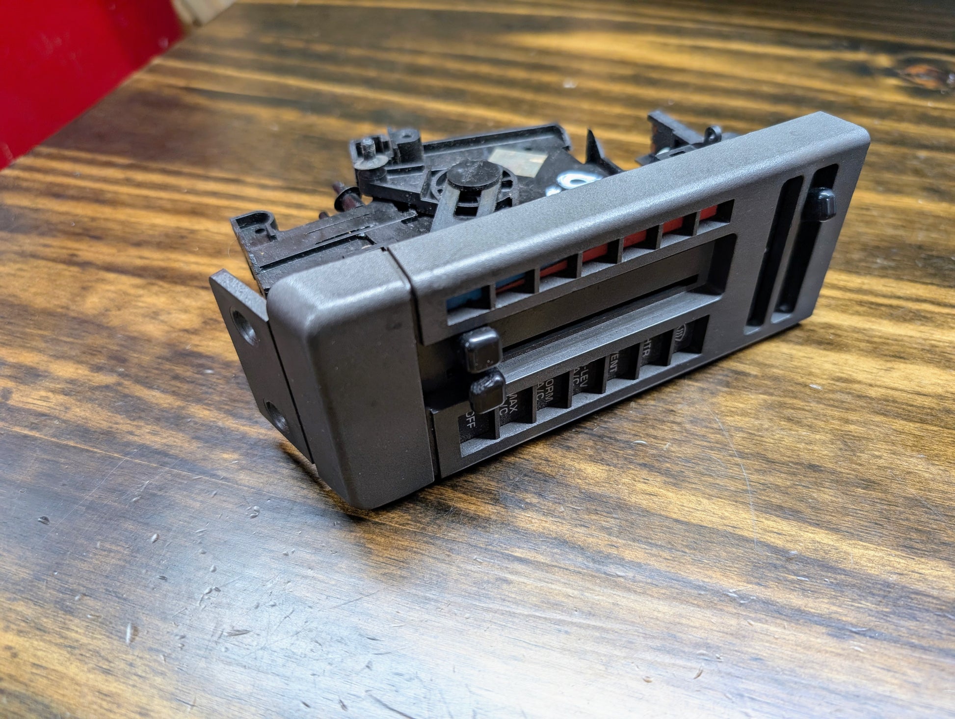 A General Motors HVAC Heater Control Panel with A/C for 1986-1994 Chevrolet S10, Blazer, and more is shown close-up on a wooden surface, featuring horizontal and vertical air vent slats with adjustment levers.