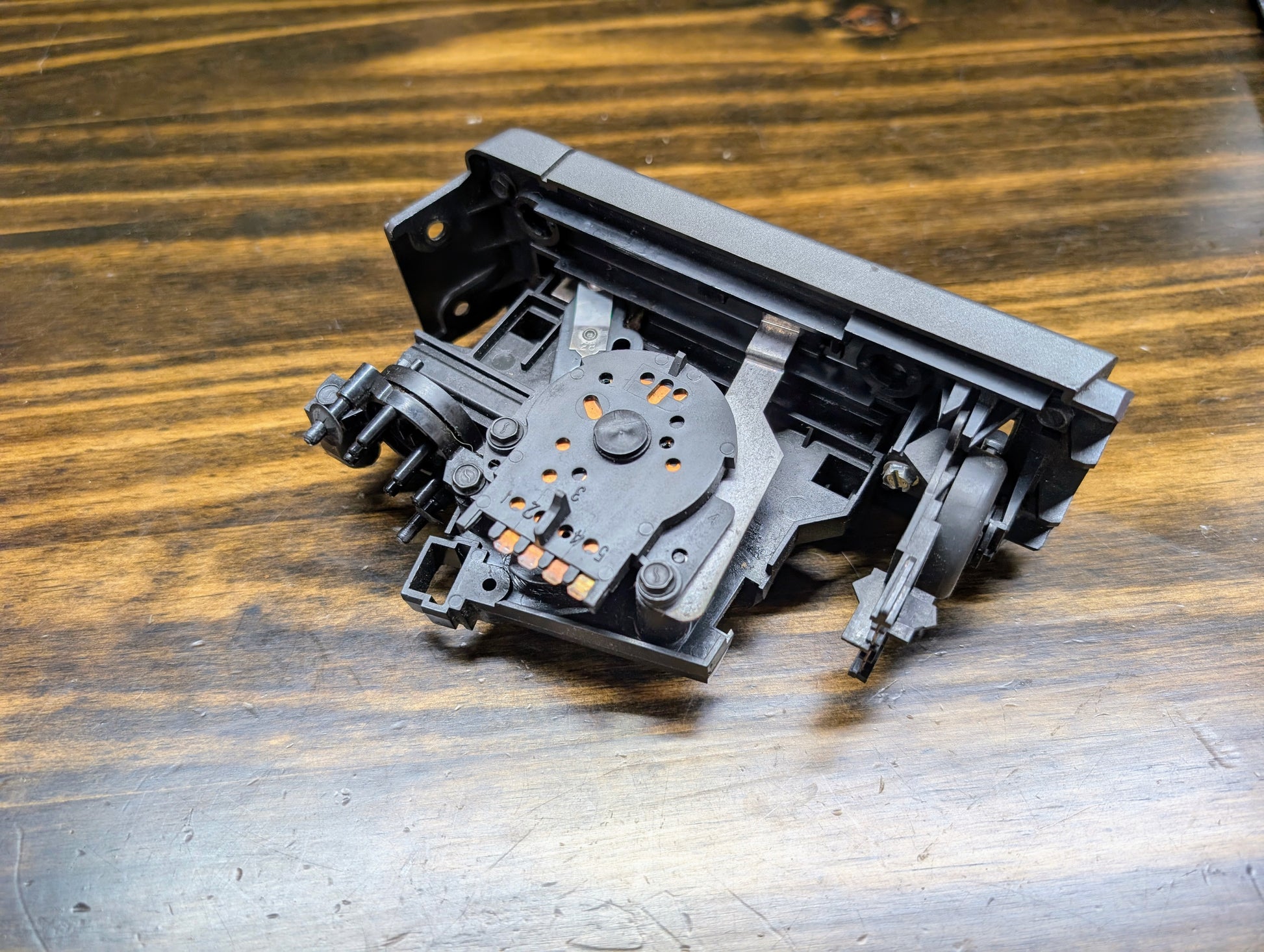 A close-up of a disassembled General Motors HVAC Heater Control Panel with A/C for 1986-1994 Chevrolet S10, Blazer, and more, shown on a wooden surface with visible grain.