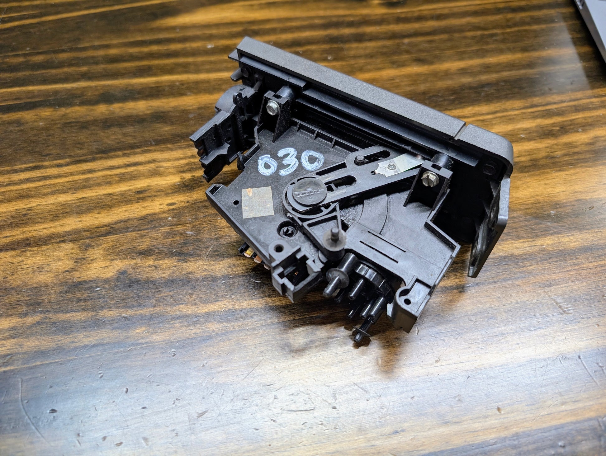 A close-up shows a General Motors HVAC Heater Control Panel with A/C for 1986-1994 Chevrolet S10 and Blazer, featuring attached gears and levers, resting on a wooden surface.