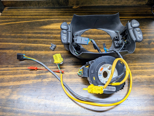 General Motors KIT Steering Wheel Black Button Radio Controls & Clock Spring for 2004-2005 Chevy S10, Blazer, and more are disassembled on a wooden surface with buttons, connectors, clock spring, and wiring visible.