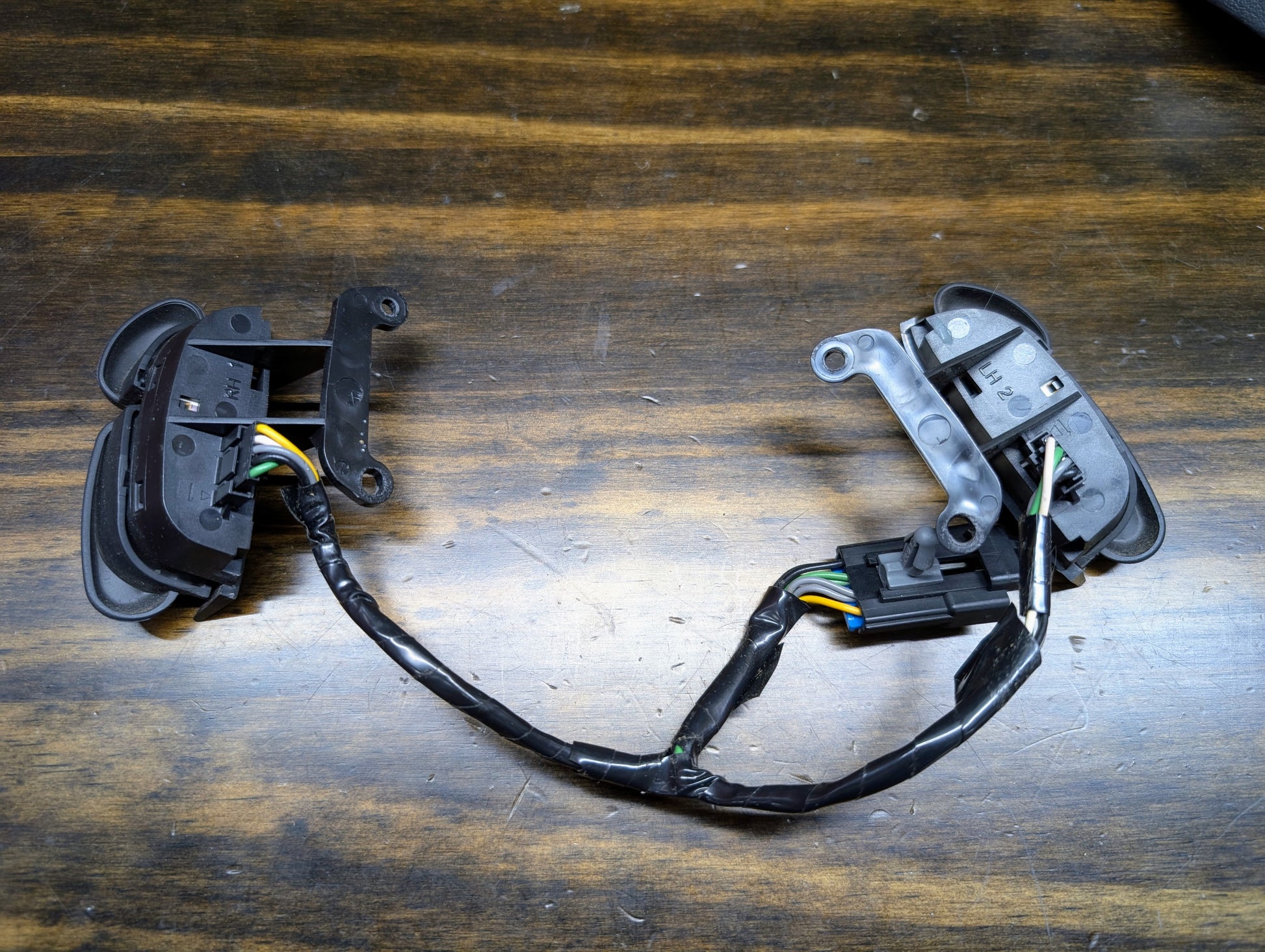 A KIT Steering Wheel Black Button Radio Controls & Clock Spring for 2004-2005 Chevy S10, Blazer, and more by General Motors rests disassembled on a wooden surface, with bundled wires connecting the components.