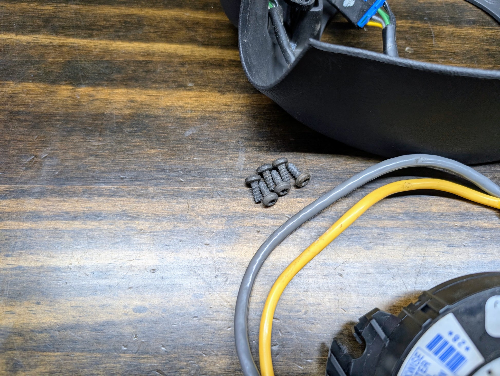 A close-up of four black screws, gray and yellow cables, a black component, and a General Motors KIT Steering Wheel Radio Controls & Clock Spring for 1999 Chevy S10, Blazer, and more—perfect for steering wheel radio control repairs.