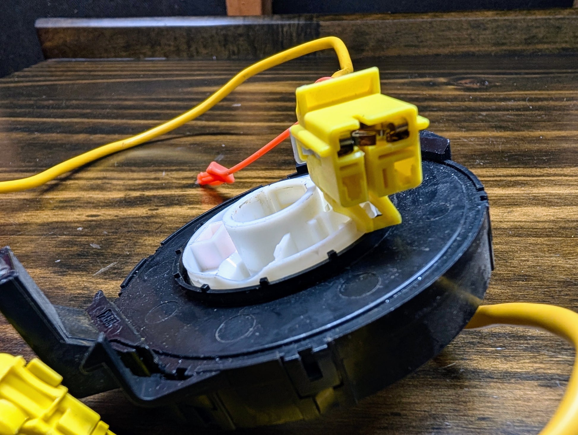 A close-up of a General Motors OEM Steering Wheel Air Bag SRS Clock Spring, tested for 2004-2005 Chevy S10 Blazer, shows its black circular housing and connectors with exposed wiring on a wooden surface.