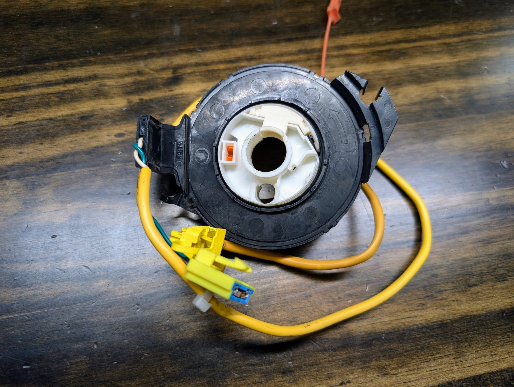 A General Motors OEM SRS clock spring for 2000-2003 Chevy S10 Blazer, with yellow/orange wires and plastic connectors, displays part numbers 26088306, 26087310, and 26083473 along with directional symbols on its black housing.
