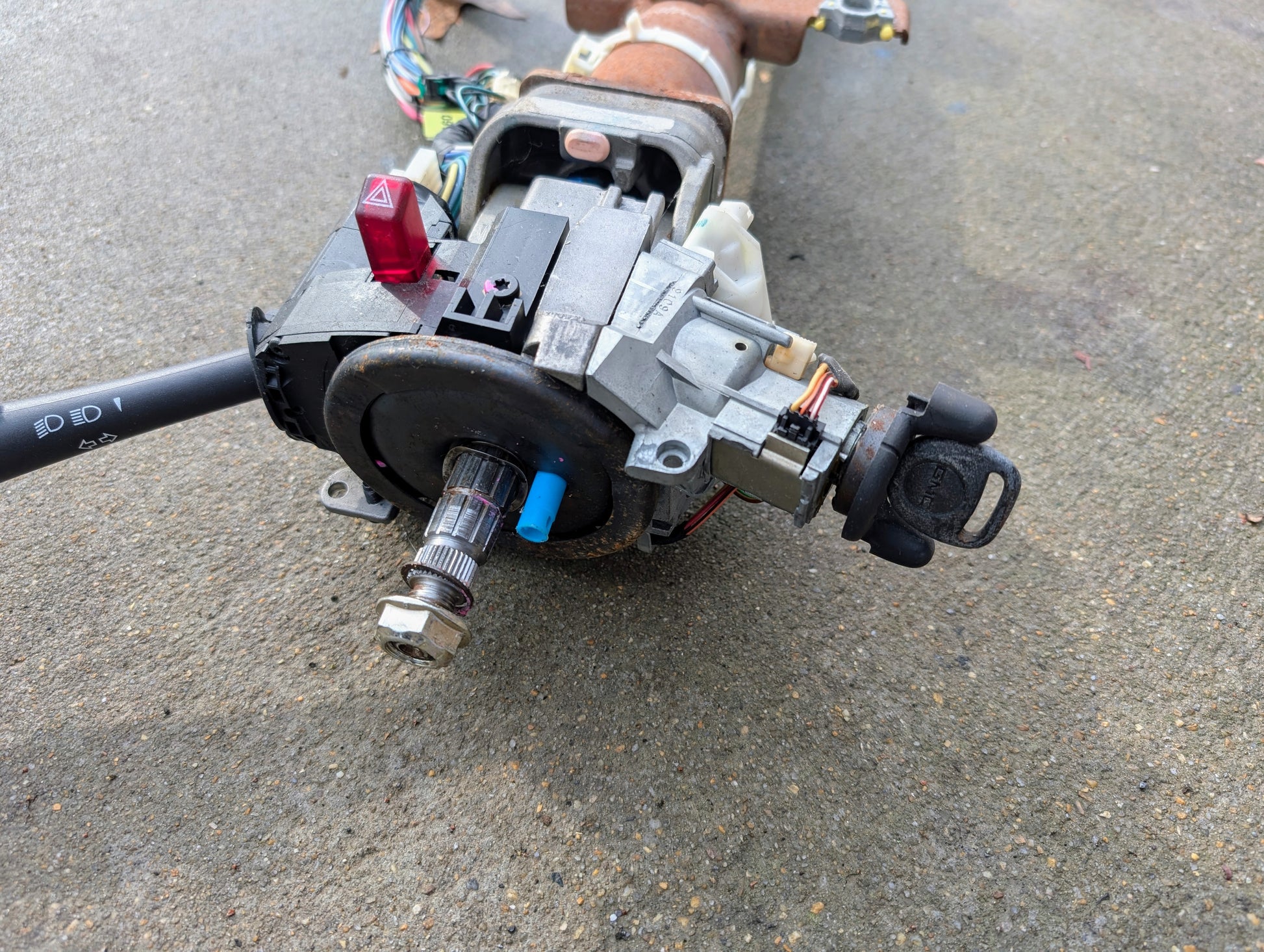 A close-up of a disassembled General Motors OEM Steering Column w/Tilt, Cruise Control, and Console Shift for 1998-2005 Chevy S10 Blazer, showing its wiring and components on concrete.