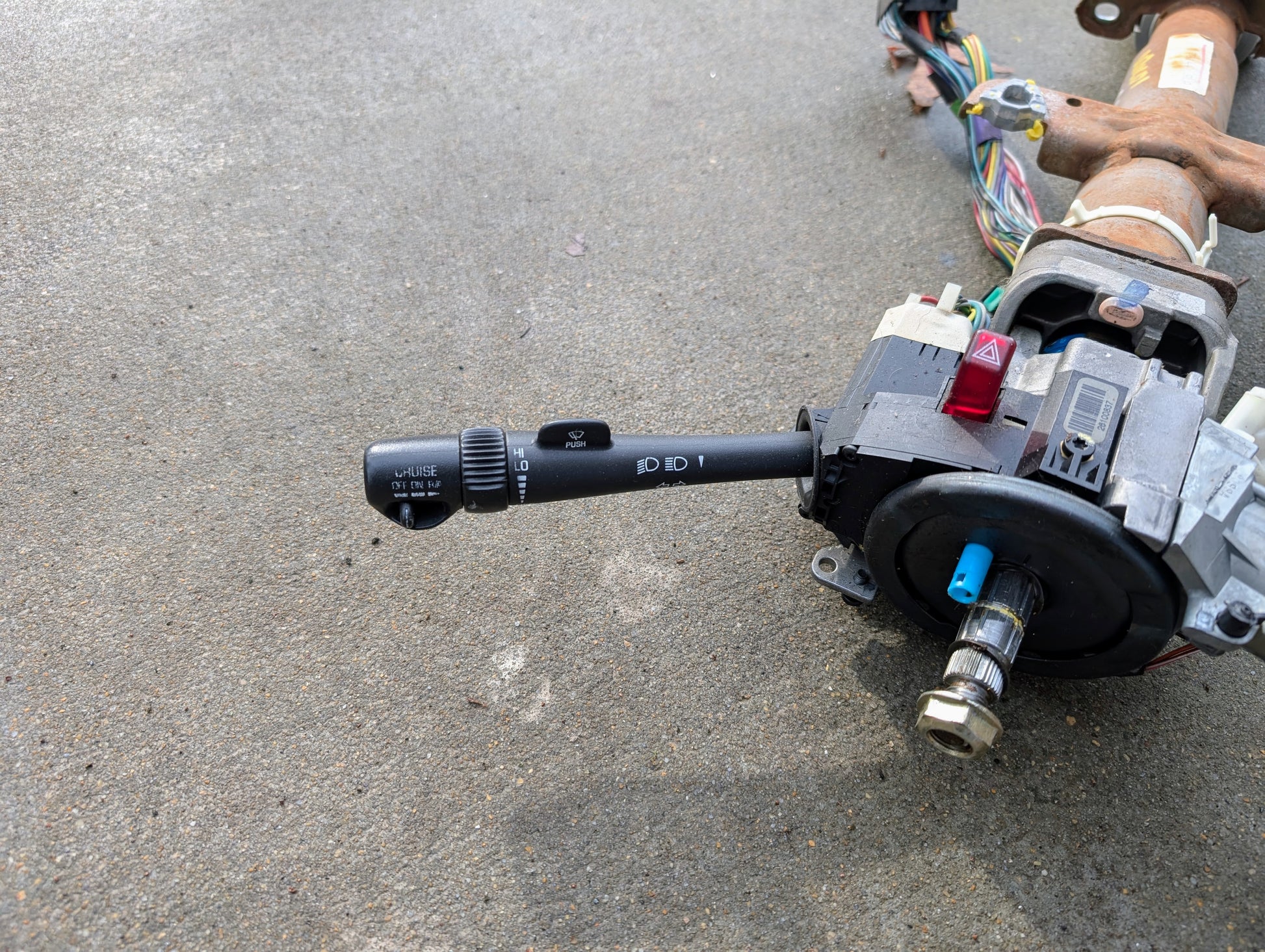 A General Motors OEM Steering Column with tilt, cruise control, and console shift for 1998-2005 Chevy S10 Blazer and more, shown with wiring and turn signal lever on a concrete surface.
