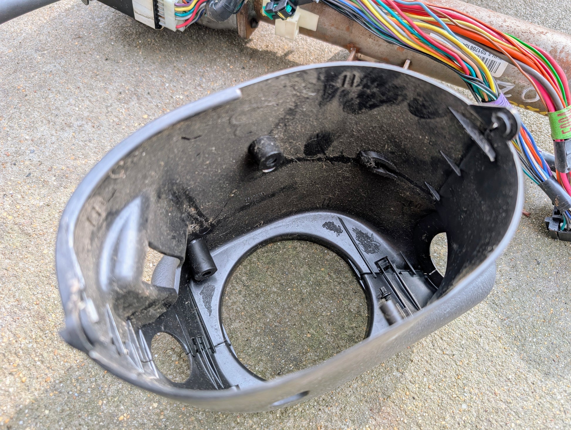 Close-up of a black General Motors OEM Steering Column w/Tilt, Cruise Control, and Console Shift for 1998-2005 Chevy S10 Blazer, shown with internal attachment points and background wiring harnesses on concrete.