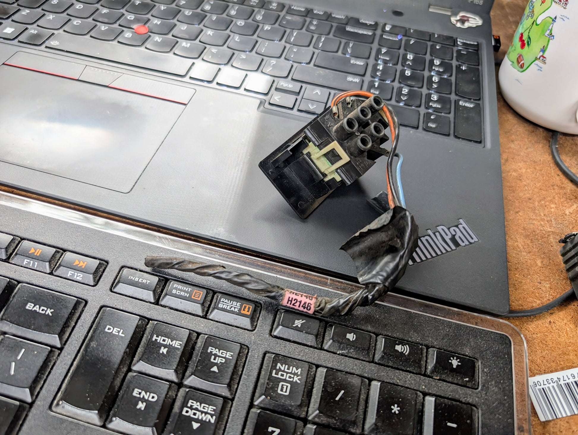 A black power drill bit, a small wired electrical component, part of a mug, and a General Motors OEM Driver LH Power Door Lock Switch for 1991-1994 Chevy S10 Blazer rest on two overlapping keyboards: a Lenovo ThinkPad laptop and another keyboard.