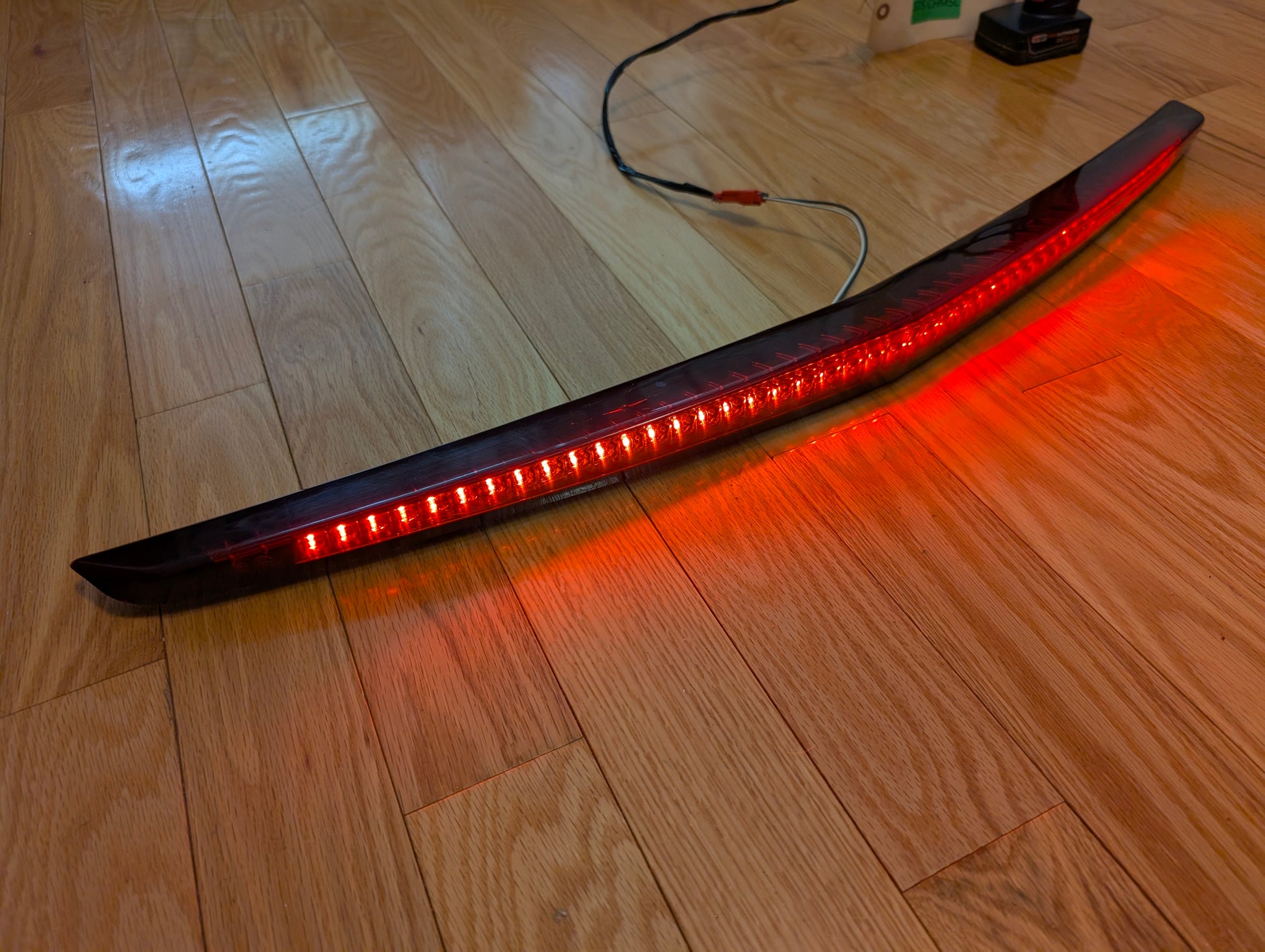 An illuminated OEM 2008-2013 Cadillac CTS Rear Stop Third Brake Light by General Motors lies on a wooden floor with visible wires, highlighting this tested CHMSL trunk lamp as a crucial exterior part for your CTS.
