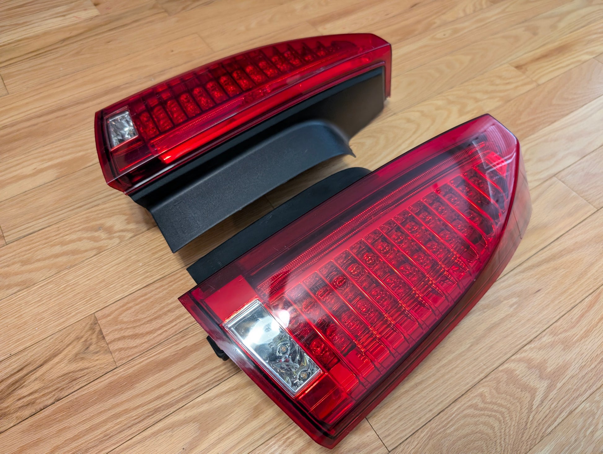 A pair of OEM left and right tail light brake lenses for 2008-2013 Cadillac CTS by General Motors are shown side by side on a light wood floor, displaying both inner and outer sides—ideal for replacement or upgrade.