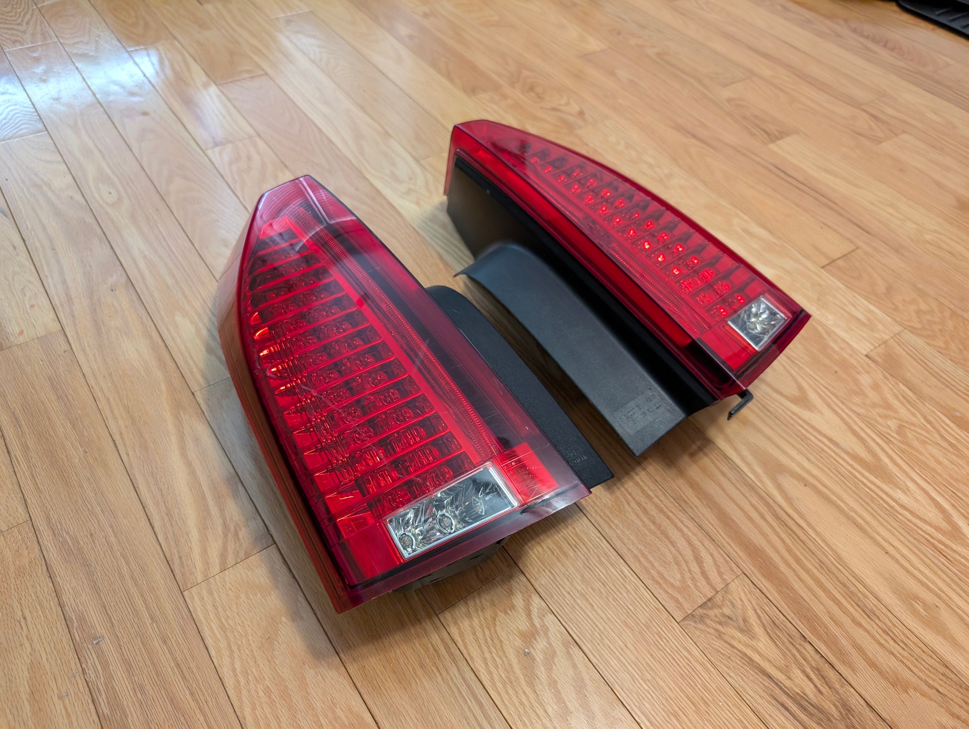 A pair of OEM left and right tail light lamp brake lenses by General Motors for 2008-2013 Cadillac CTS are placed side by side on a hardwood floor, ideal as a tested rear lamp replacement.