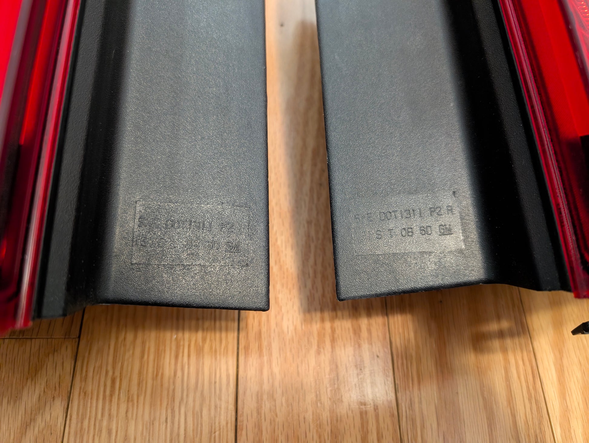 A pair of General Motors OEM left and right tail light lamp brake lenses for 2008–2013 Cadillac CTS, black plastic with red upper detailing and faint molded text, are side by side on a wooden surface.