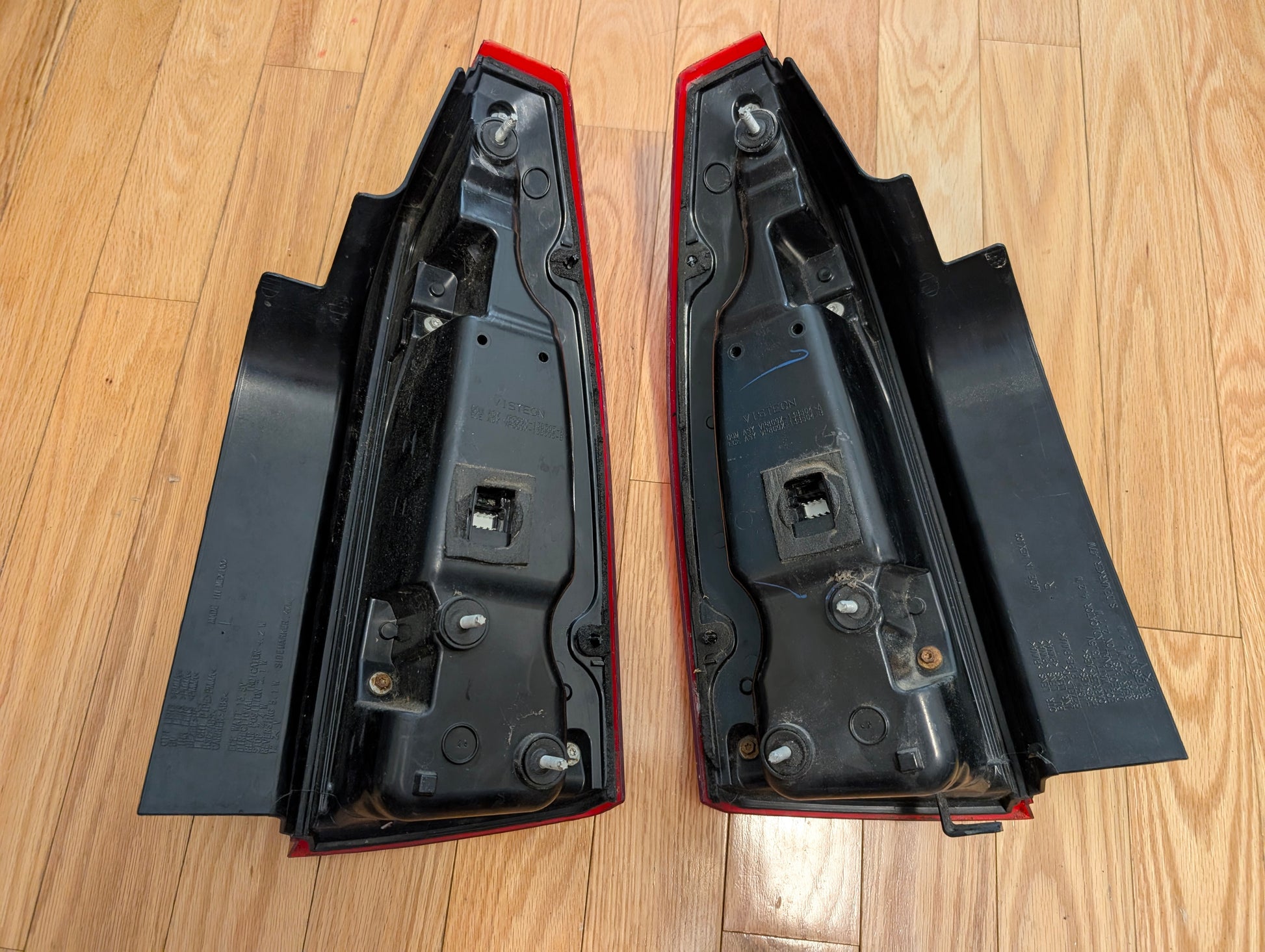 A pair of General Motors OEM left and right tail light brake lens assemblies for 2008-2013 Cadillac CTS are shown side by side with mounting bolts and connectors visible, suitable for rear lamp or brake assembly replacement.