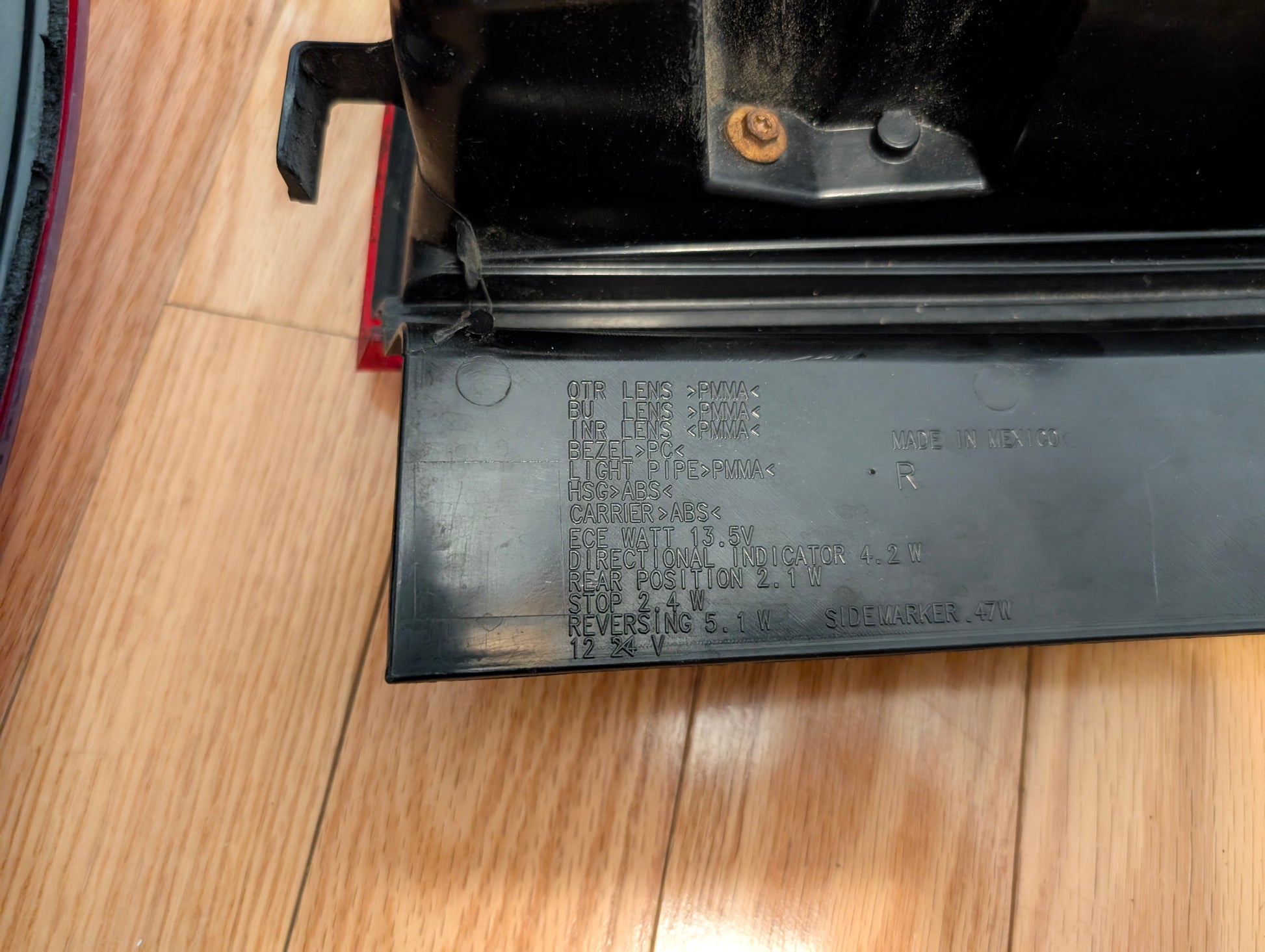 A close-up of a General Motors OEM left and right tail light lamp brake lens for 2008-2013 Cadillac CTS shows embossed specs and codes on the plastic part, with some dust on the assembly, placed on a wooden floor.