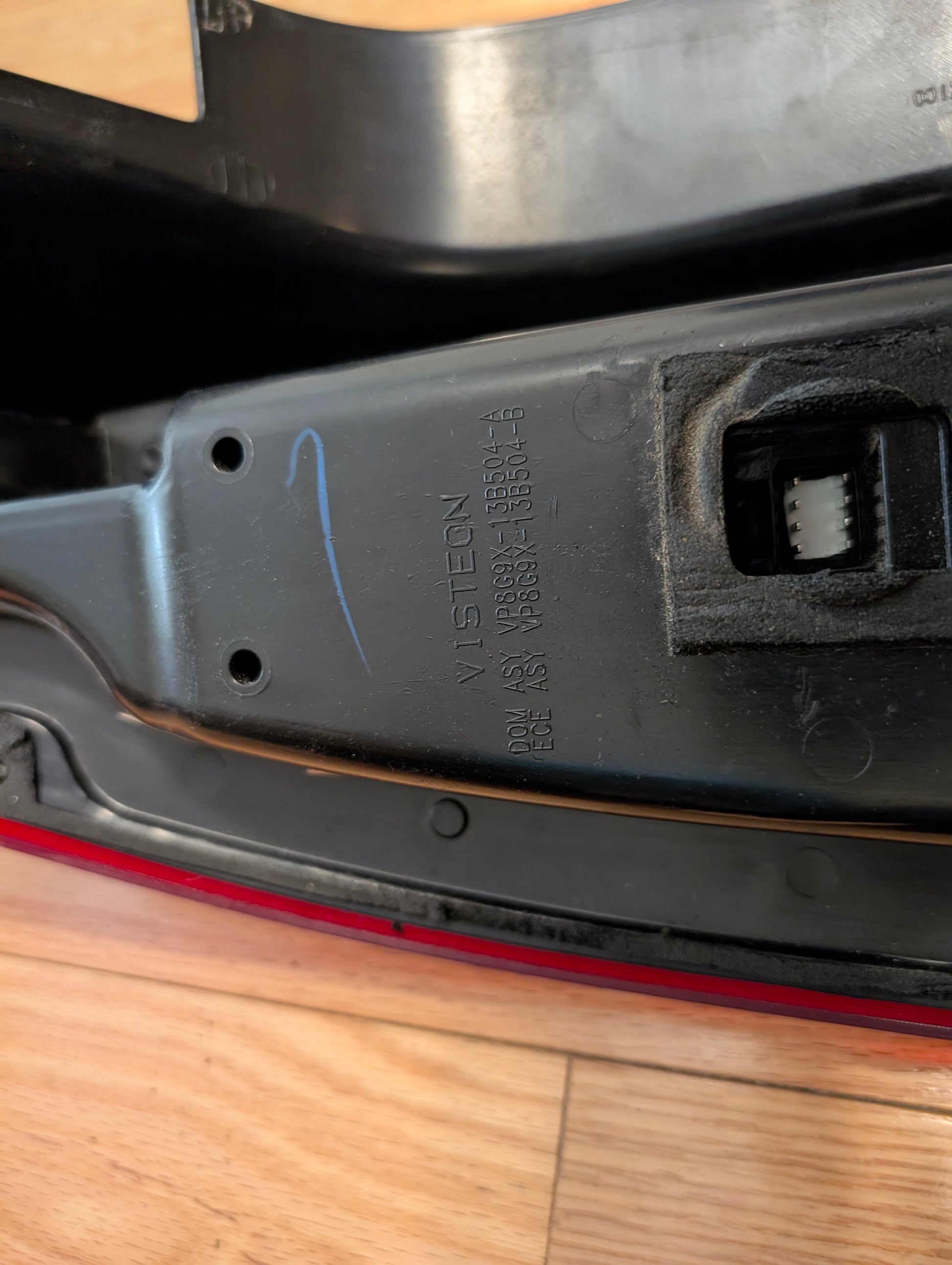 Close-up of a General Motors OEM left and right tail light brake lens assembly for 2008-2013 Cadillac CTS, featuring black plastic housing, visible identification numbers, blue mark, and white connector resting on a wooden surface.