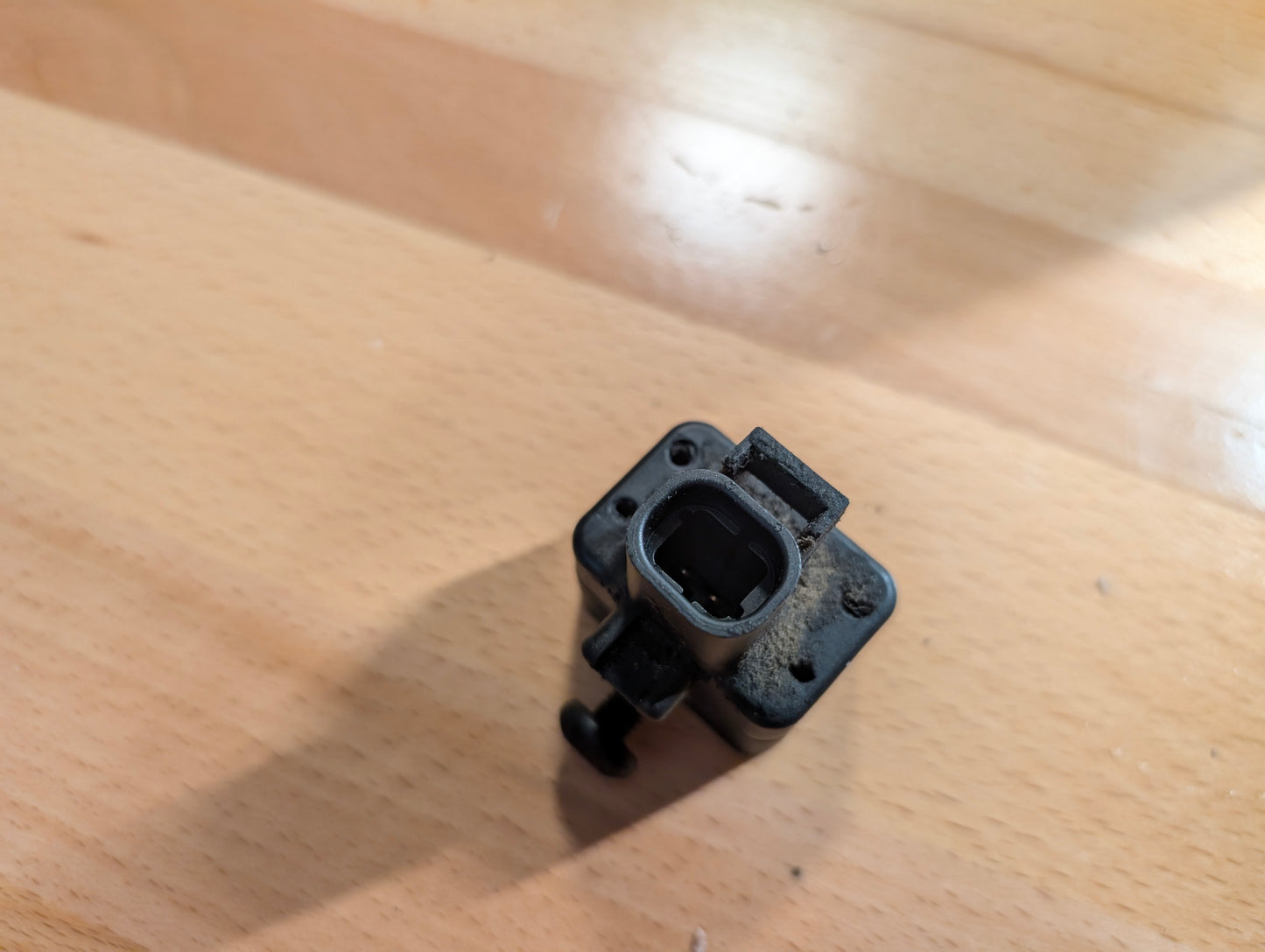 A close-up of a small, rectangular OEM Front Impact Air Bag Sensor 15750627 by General Motors for 2003-2004 Chevy Express and GMC Savanna, resting on a light wood surface.