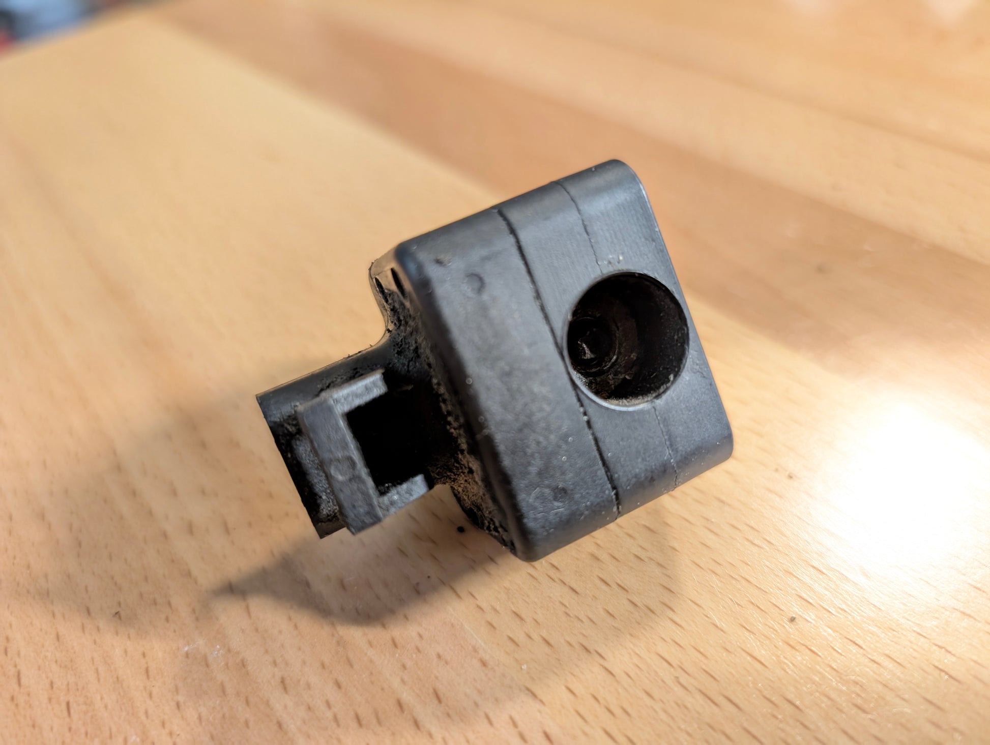 A close-up of a small black plastic OEM Front Impact Air Bag Sensor 15750627 by General Motors, featuring a cylindrical hole and rectangular protrusion, for 2003-2004 Chevy Express or GMC Savana, on a light wooden surface.