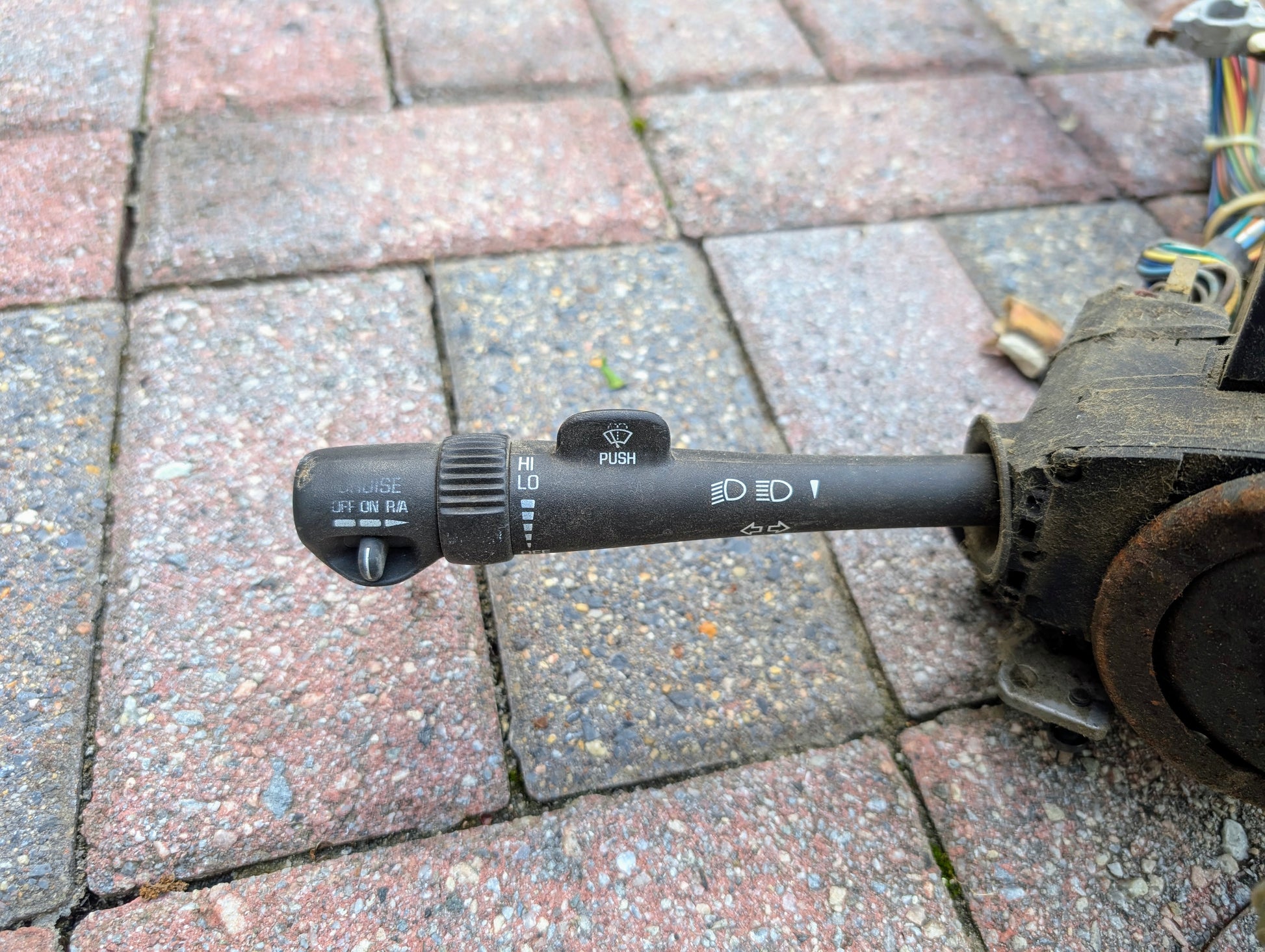 A close-up of a General Motors OEM Steering Column with tilt, cruise control, and column shift for 1998–2005 Chevy S10 Blazer shows lever assembly with symbols for lights, wipers, washer, and visible wires on the right side.