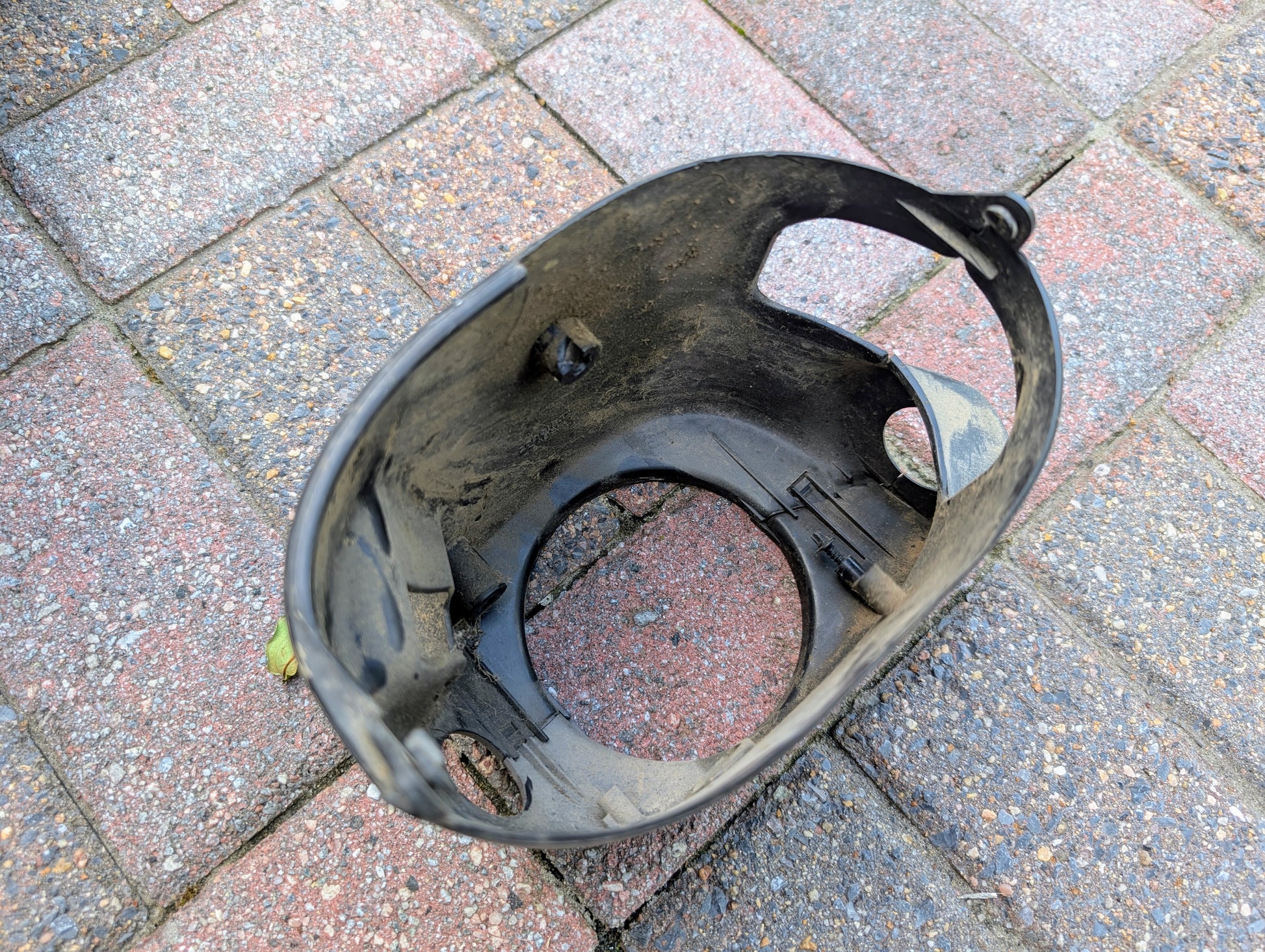 A dirty, black OEM General Motors steering column with tilt, cruise control, and column shift for 1998-2005 Chevy S10 Blazer lies on multicolored brick pavement.