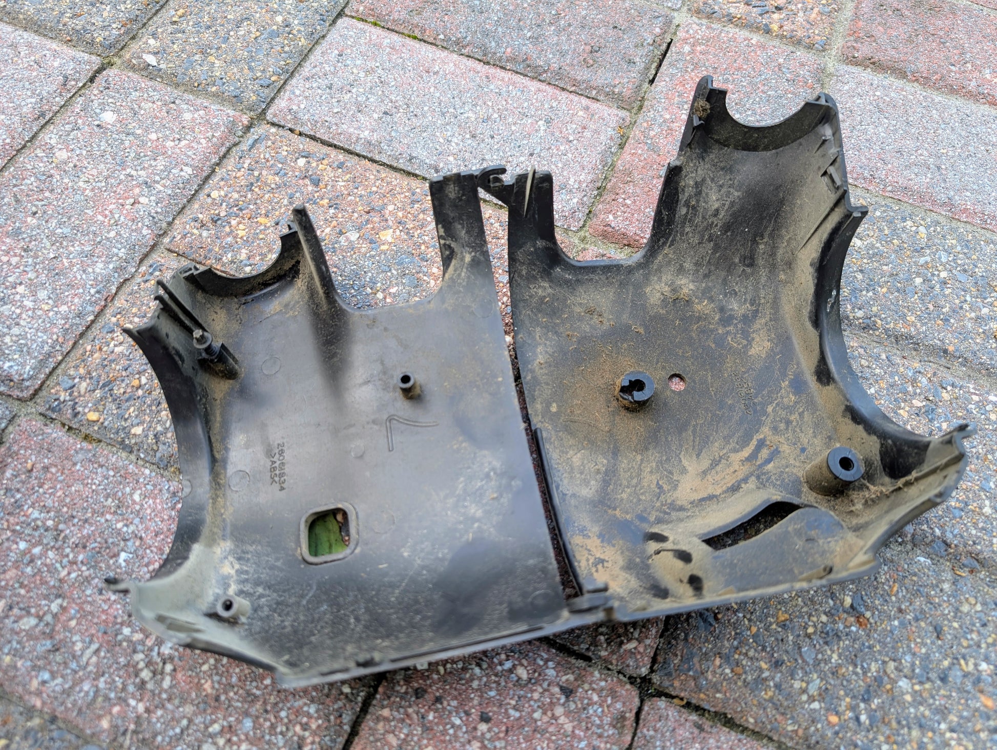 A damaged and dirty General Motors OEM Steering Column casing with tilt, cruise control, and column shift for 1998-2005 Chevy S10 Blazer lies open on a red and gray brick surface, appearing to be part of a larger device.