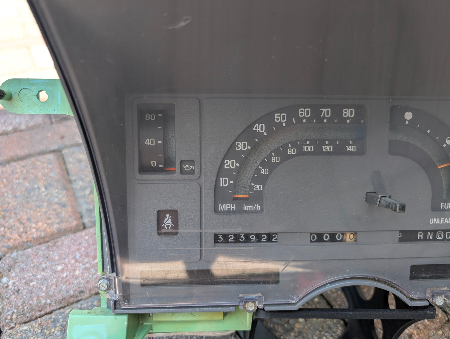 Close-up of a General Motors OEM Instrument Cluster with Mechanical Speedo & PRNDL for 1986-1989 Chevy S10 Blazer, showing speedometer, oil pressure gauge, odometer at 323922, and seatbelt light. Not installed in a vehicle.