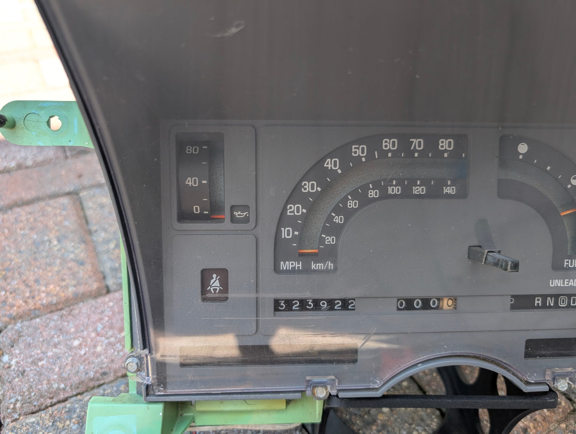 Close-up of a General Motors OEM Instrument Cluster with Mechanical Speedo & PRNDL for 1986-1989 Chevy S10 Blazer, showing speedometer, oil pressure gauge, odometer at 323922, and seatbelt light. Not installed in a vehicle.