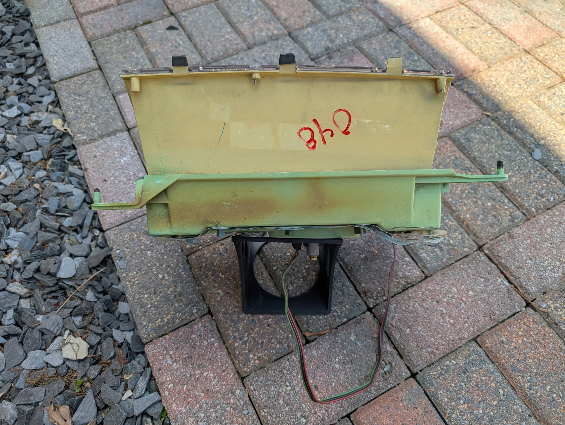 A rectangular metal and plastic OEM Instrument Cluster with Mechanical Speedo & PRNDL, labeled 840 in red and with wires attached, from General Motors for 1986–1989 Chevy S10 Blazer, sits on a brick and stone patio.