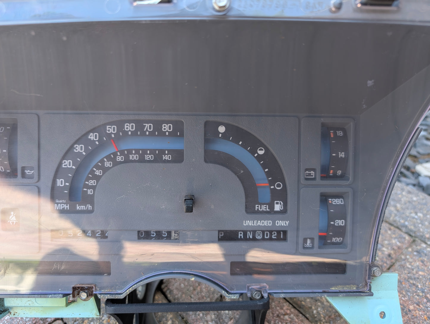 A close-up of a General Motors Low Mile 52K OEM Instrument Cluster for 1986-1994 Chevy S10 Blazer shows an analog speedometer in mph/km/h, fuel gauge (UNLEADED ONLY), PRNDL gear display, odometer at 52K, and engine temperature indicator.
