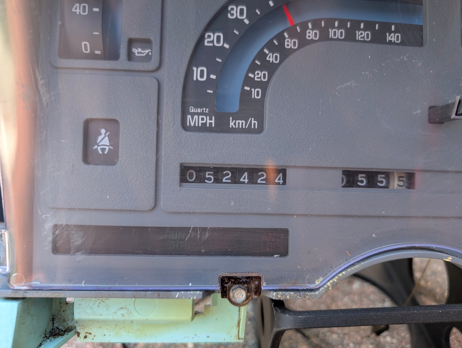 Close-up of a General Motors Low Mile 52K OEM Instrument Cluster with PRNDL for 1986-1994 Chevy S10 Blazer, showing an analog speedometer, warning lights, and odometer at 52,424 miles; dashboard cover has minor scratches.