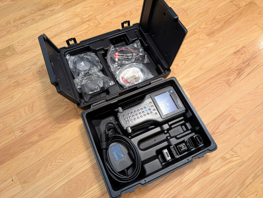 A rugged black case on a wooden floor holds a Vetronix TESTED Tech 2 Automotive Diagnostic Tool & Accessories for 1991-2013 GM Vehicles, including screen, cables, connectors, and accessories arranged in molded compartments.