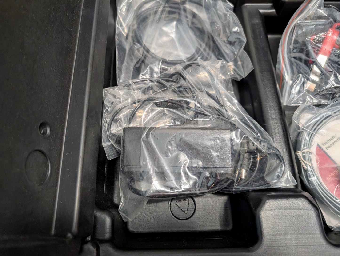 A Vetronix TESTED Tech 2 Automotive Diagnostic Tool & Accessories for 1991-2013 GM vehicles is sealed in a clear plastic bag and stored in a black case with coiled cables and other electronic accessories.