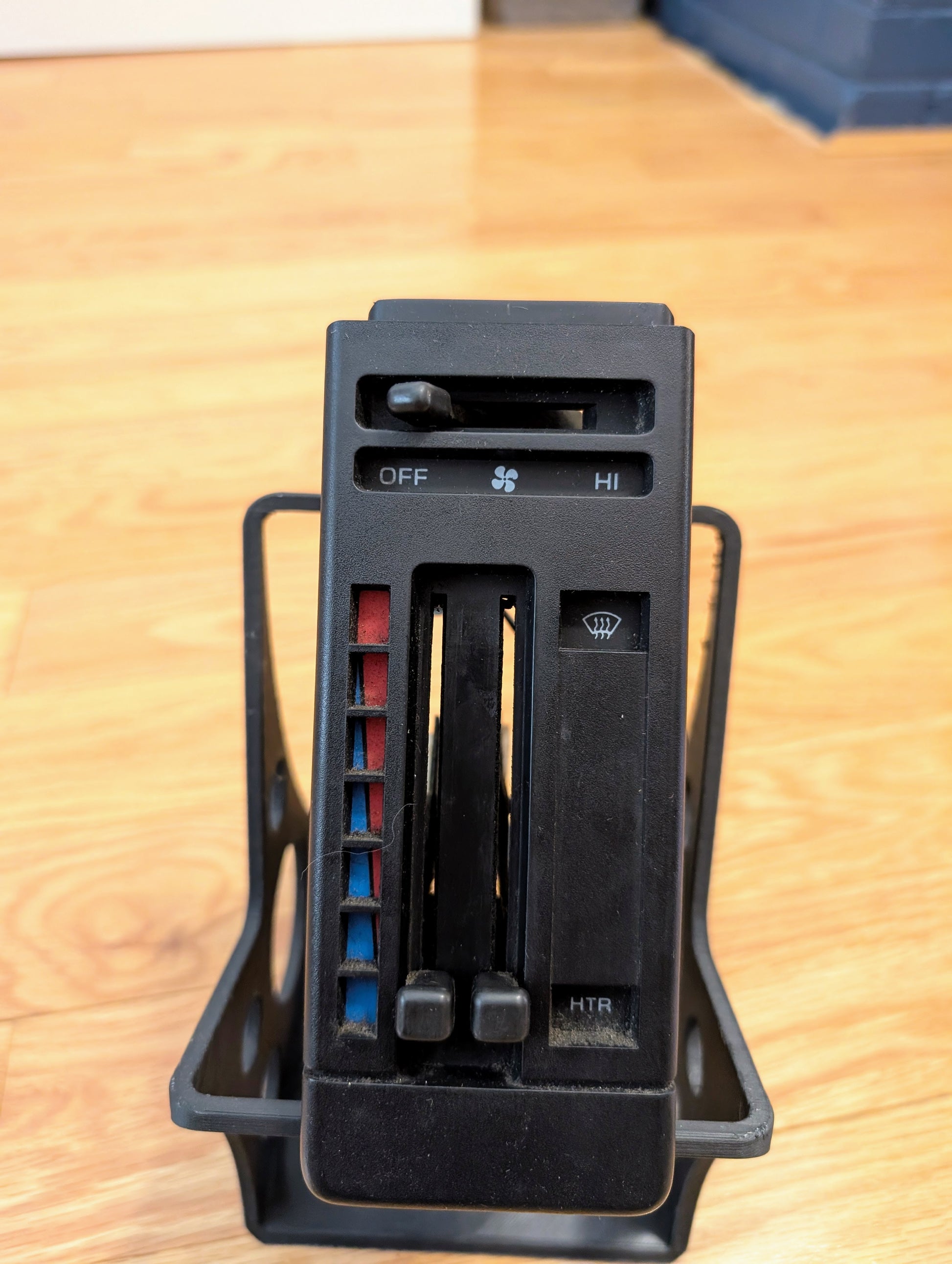 Close-up of General Motors RARE HVAC Heater Control Panel OEM (NO A/C, NO Vent) for 1986-1994 Chevrolet S10, Blazer & more, featuring sliders for fan speed and temperature. The unit rests on a light wood surface.