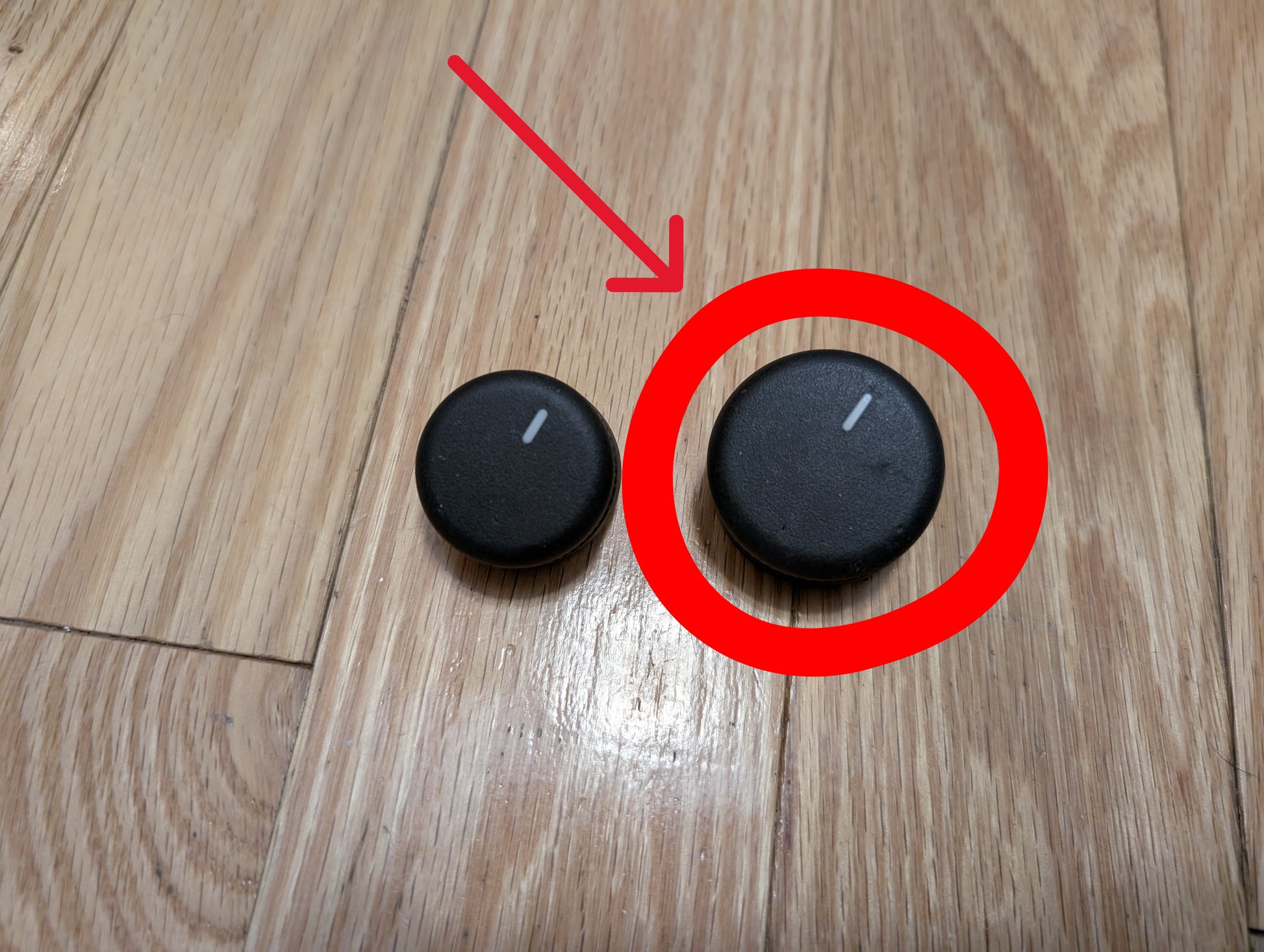 Two round black General Motors SET Heater Climate Control Switch Knobs, compatible with the 2002 Cadillac Escalade and more, rest on a wooden floor. The right knob is circled in red and indicated by a red arrow.