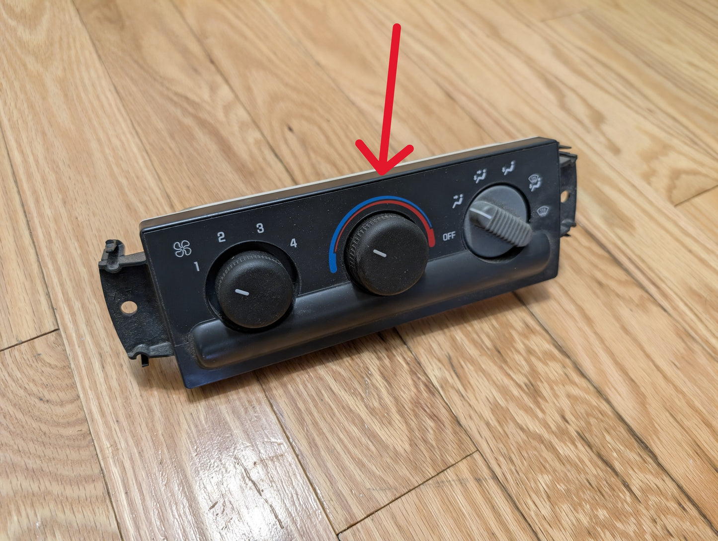 A General Motors SET Heater Climate Control Switch Knobs for 2002 Cadillac Escalade sits on a wooden floor. A red arrow highlights the central dial, displaying a blue-to-red temperature range and set to cold.