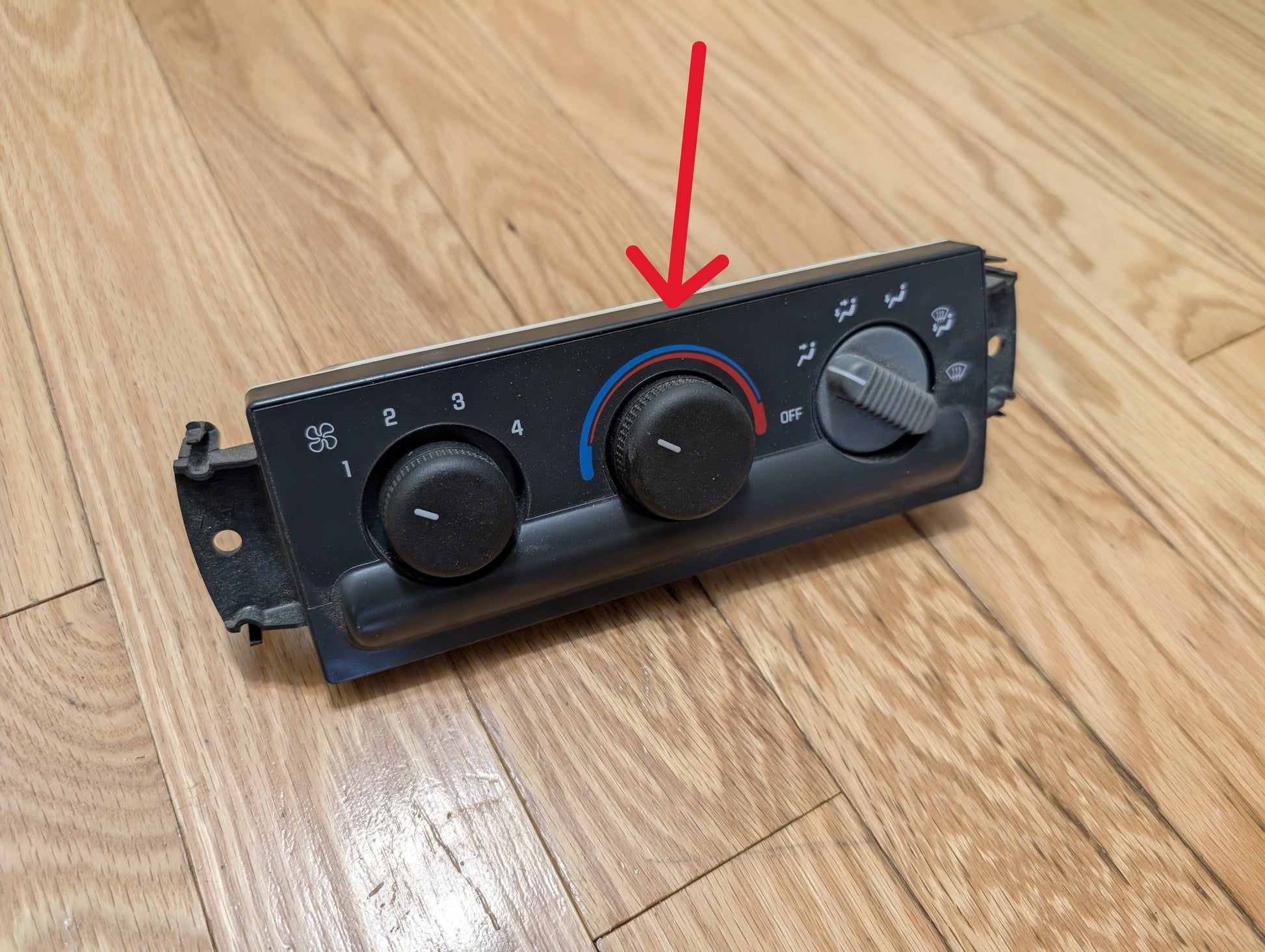 A General Motors SET Heater Climate Control Switch Knobs for 2002 Cadillac Escalade sits on a wooden floor. A red arrow highlights the central dial, displaying a blue-to-red temperature range and set to cold.