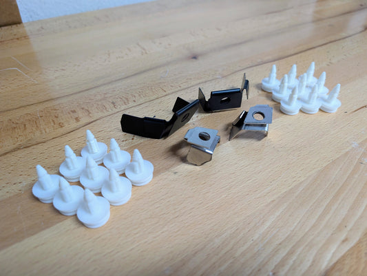 Several white plastic fasteners and three metal clips from The Ugly Truckling KIT Door Panel Armrest Repair w/Clips for 1998-2005 Chevy S10, Blazer, GMC Sonoma, Jimmy are arranged on a light wooden surface, with the clips in the center.
